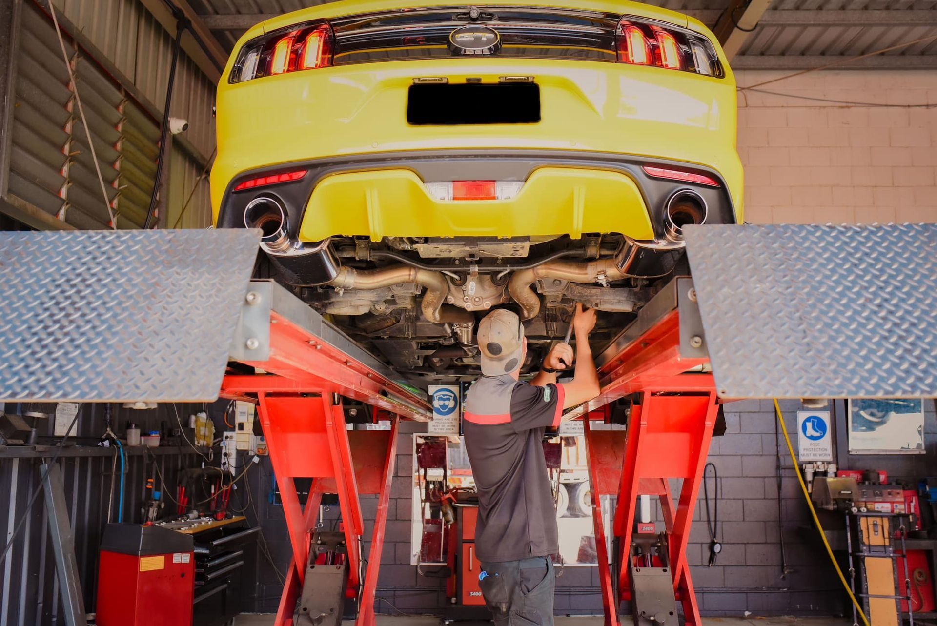 A man is working on a yellow mustang on a lift in a garage.