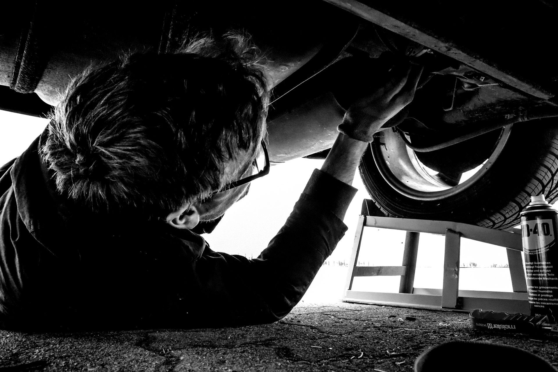 A black and white photo of a man working under a car.