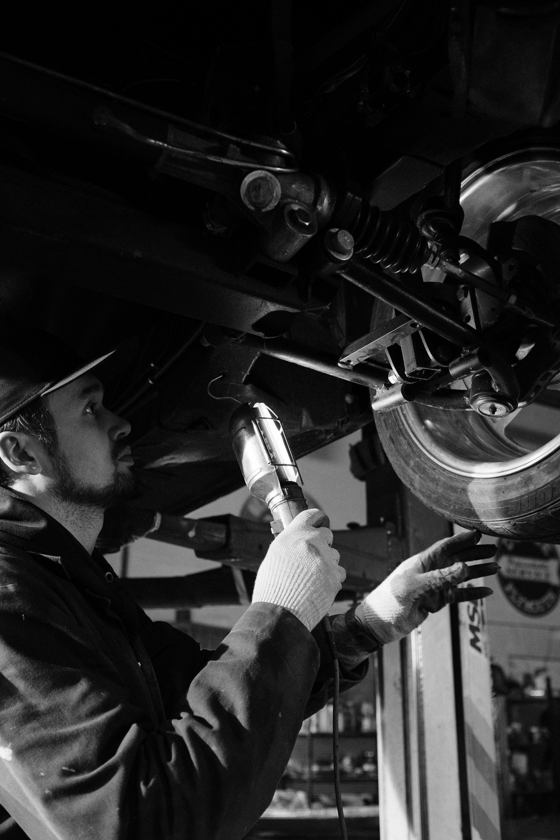 A black and white photo of a man working under a car.