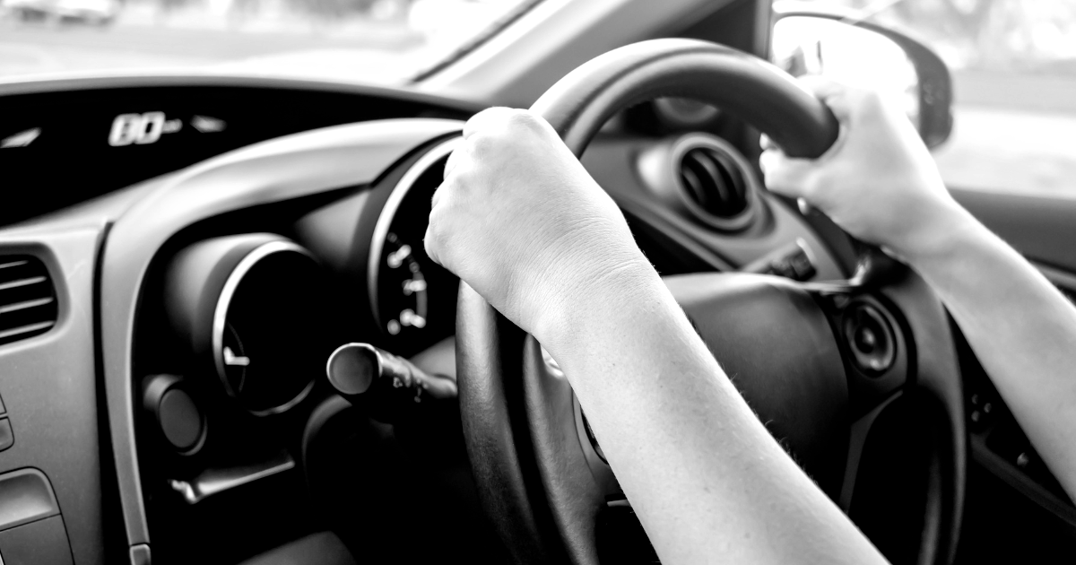 A person is driving a car with their hands on the steering wheel.