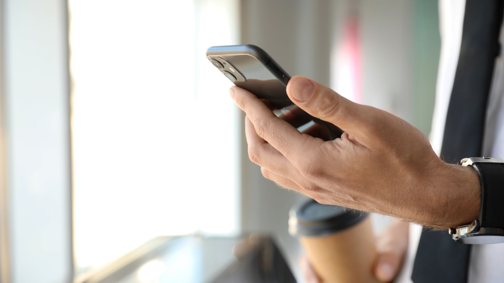 A man is holding a cup of coffee and a cell phone.