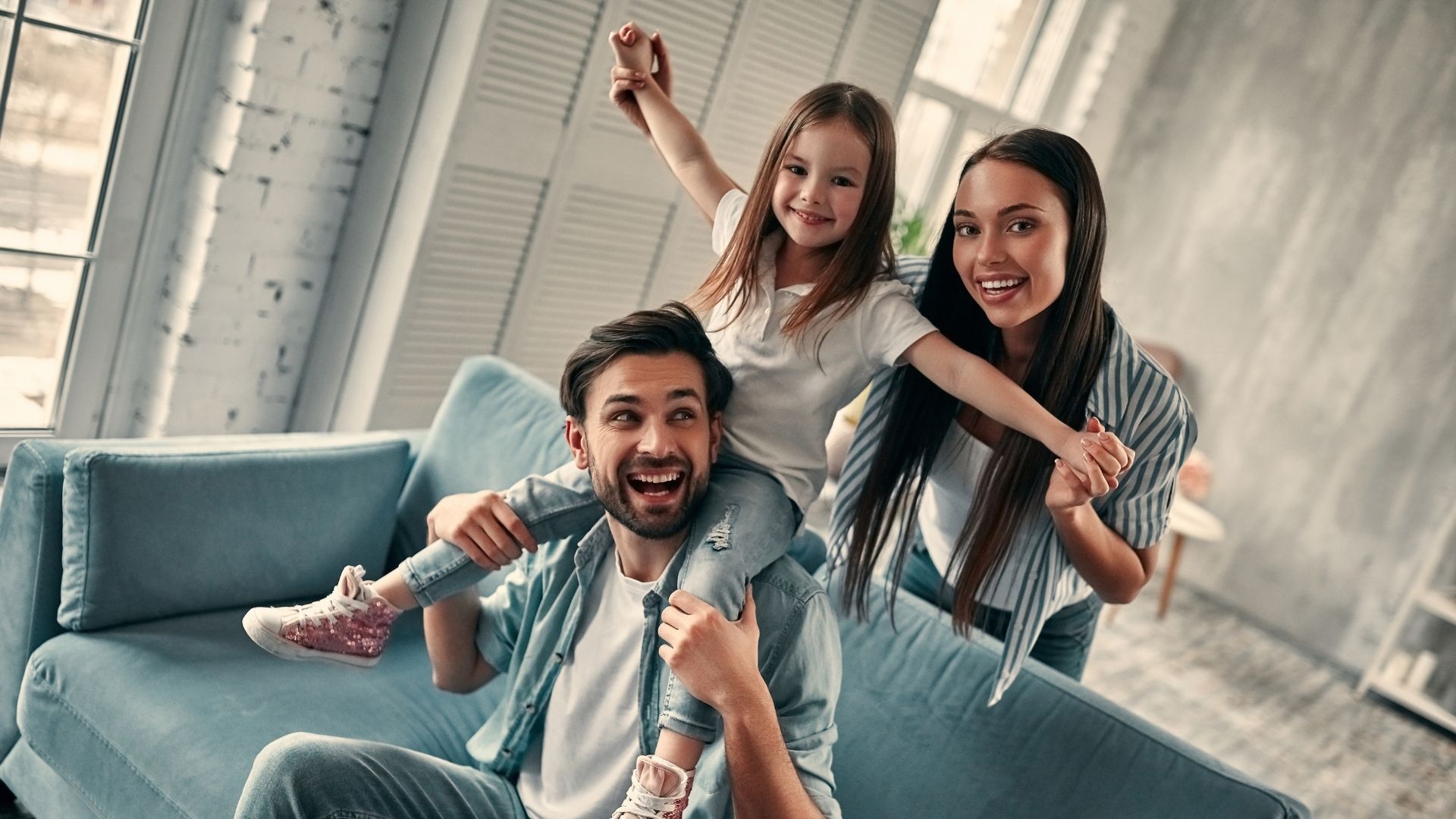 A man is sitting on a couch holding a little girl on his shoulders.