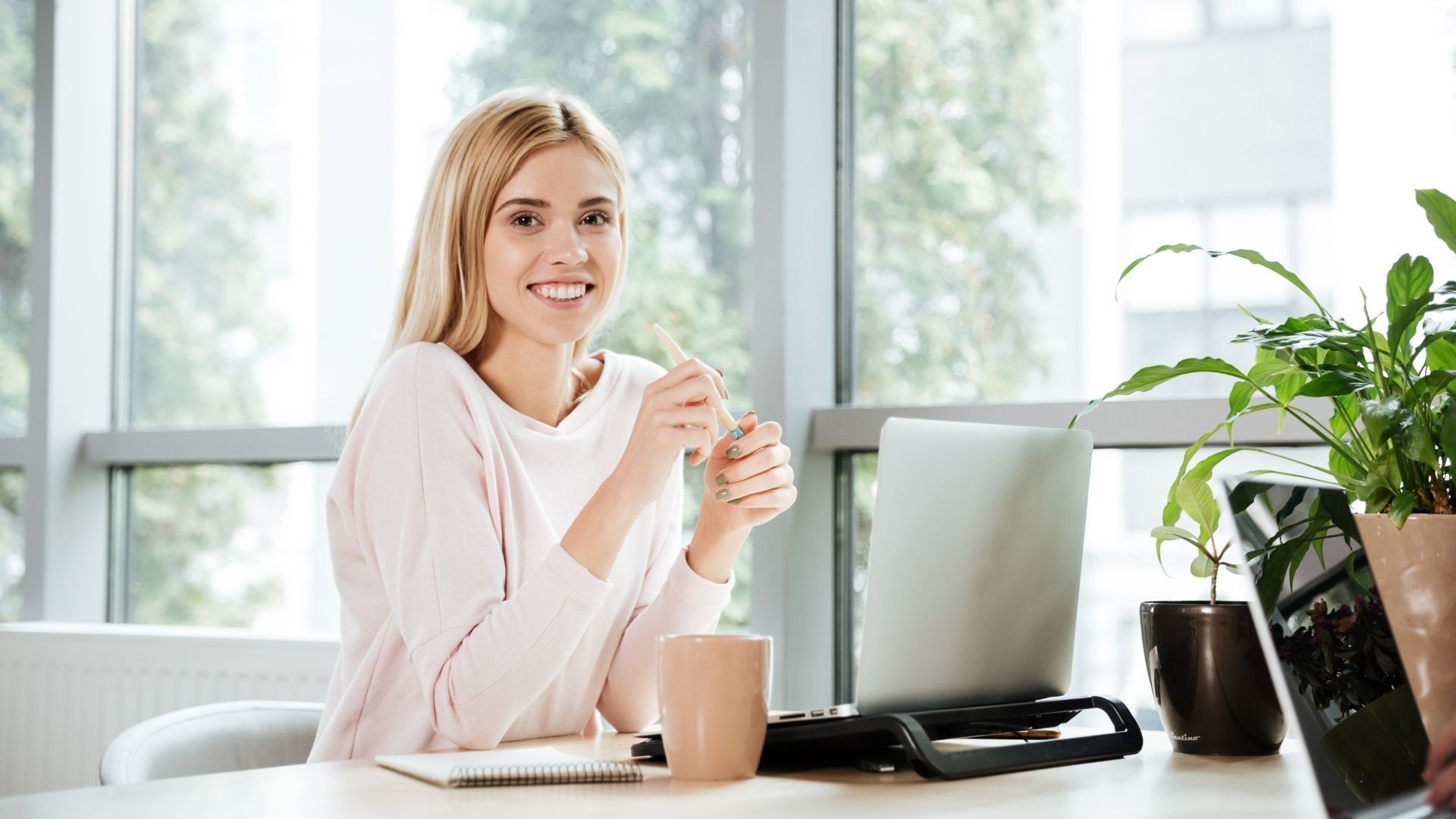 A woman is sitting at a desk with a laptop and a cup of coffee.