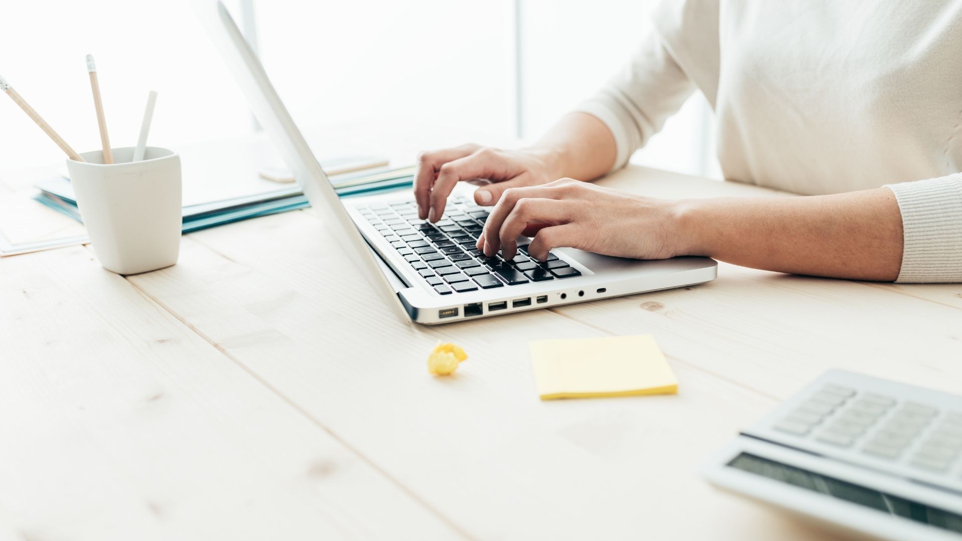 A woman is typing on a laptop computer at a desk.