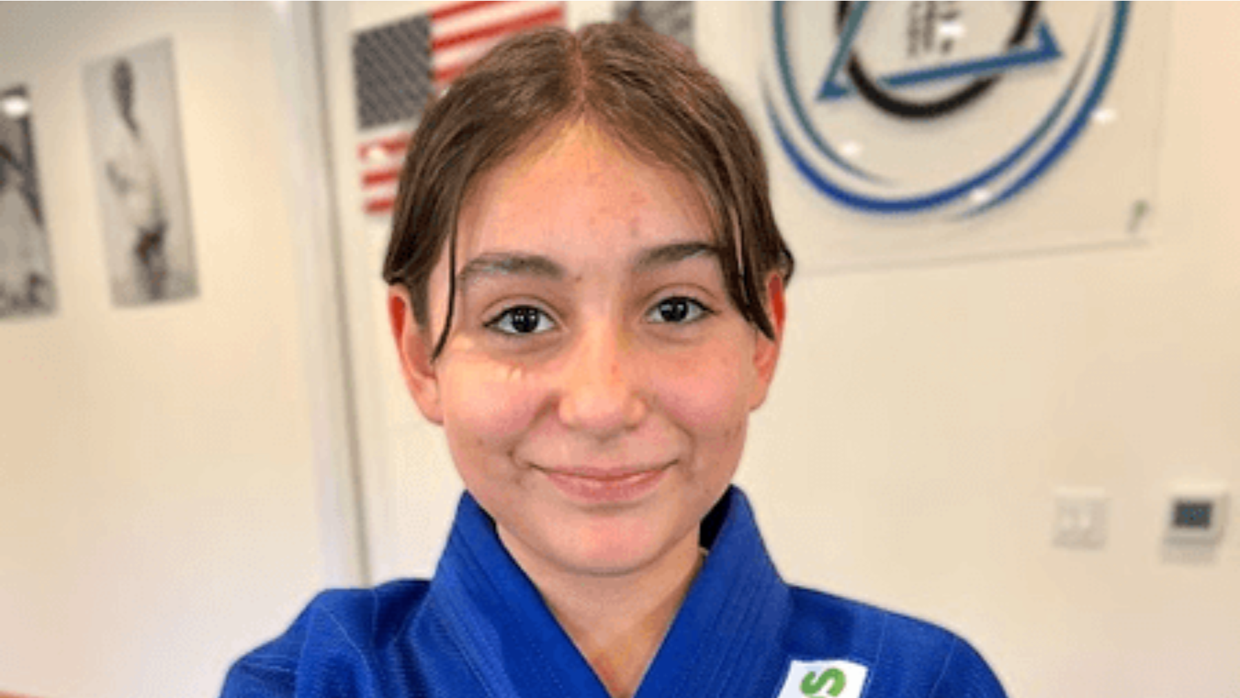 A young girl in a blue karate uniform is smiling for the camera.
