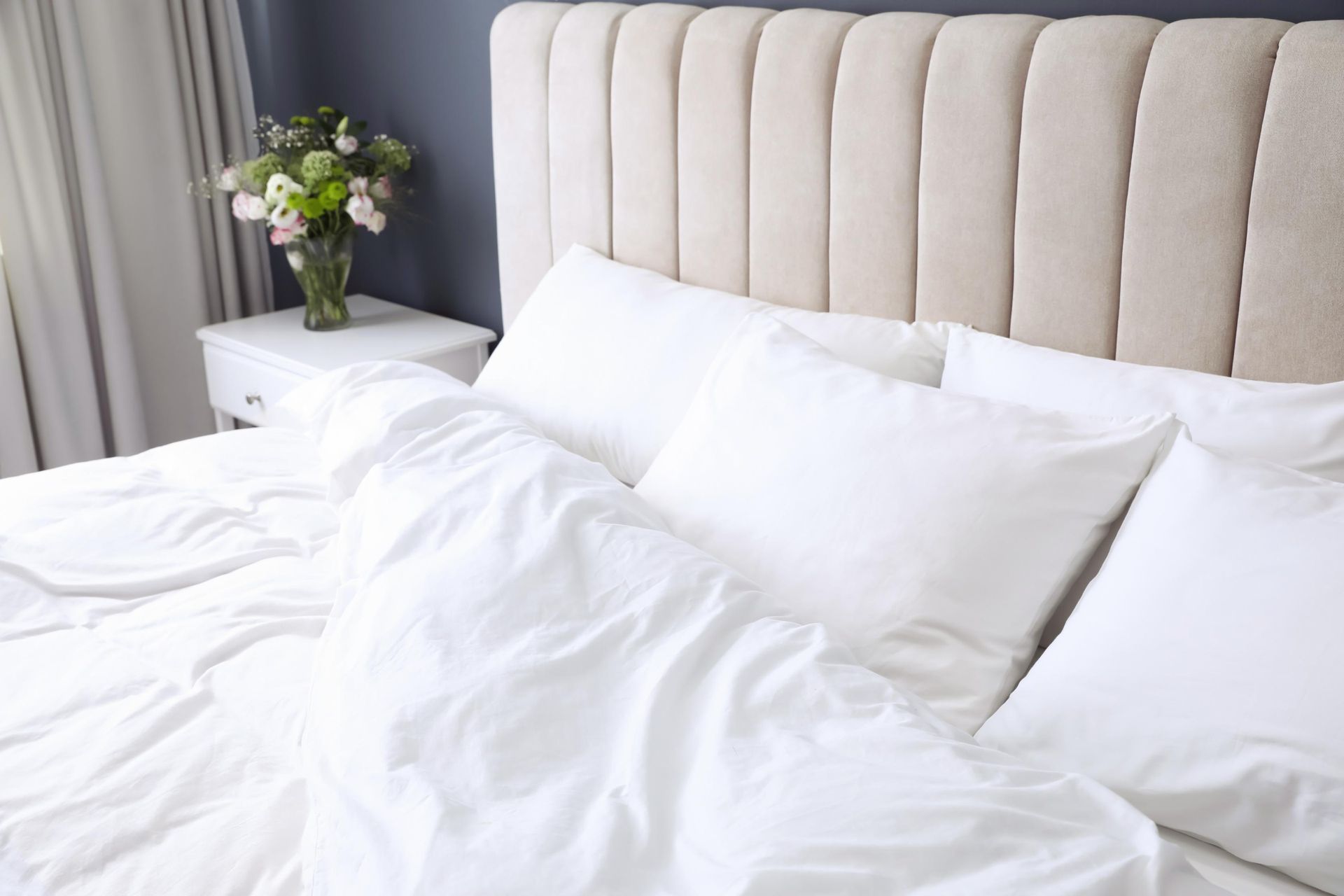 a bed with white sheets and pillows in a bedroom with a vase of flowers on the nightstand