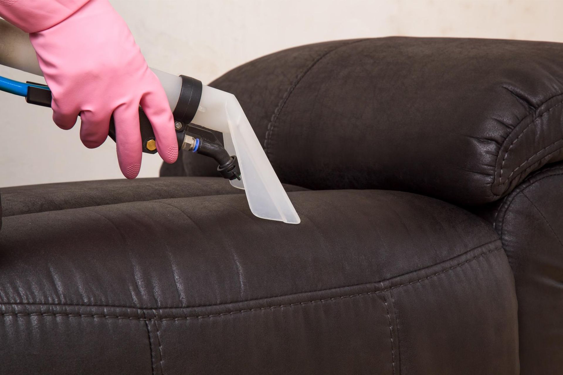 a person wearing pink gloves is cleaning a leather couch with a vacuum cleaner