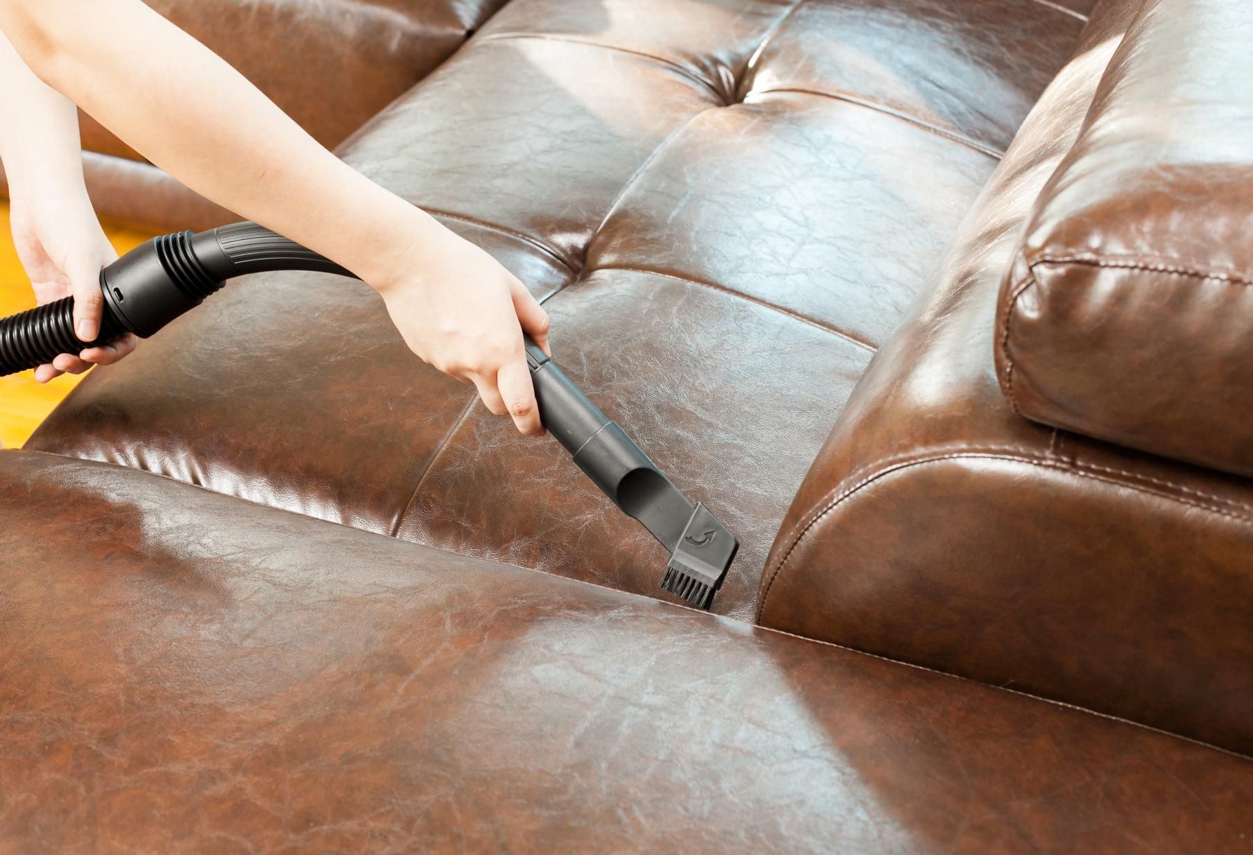 a person is vacuuming a brown leather couch with a vacuum cleaner
