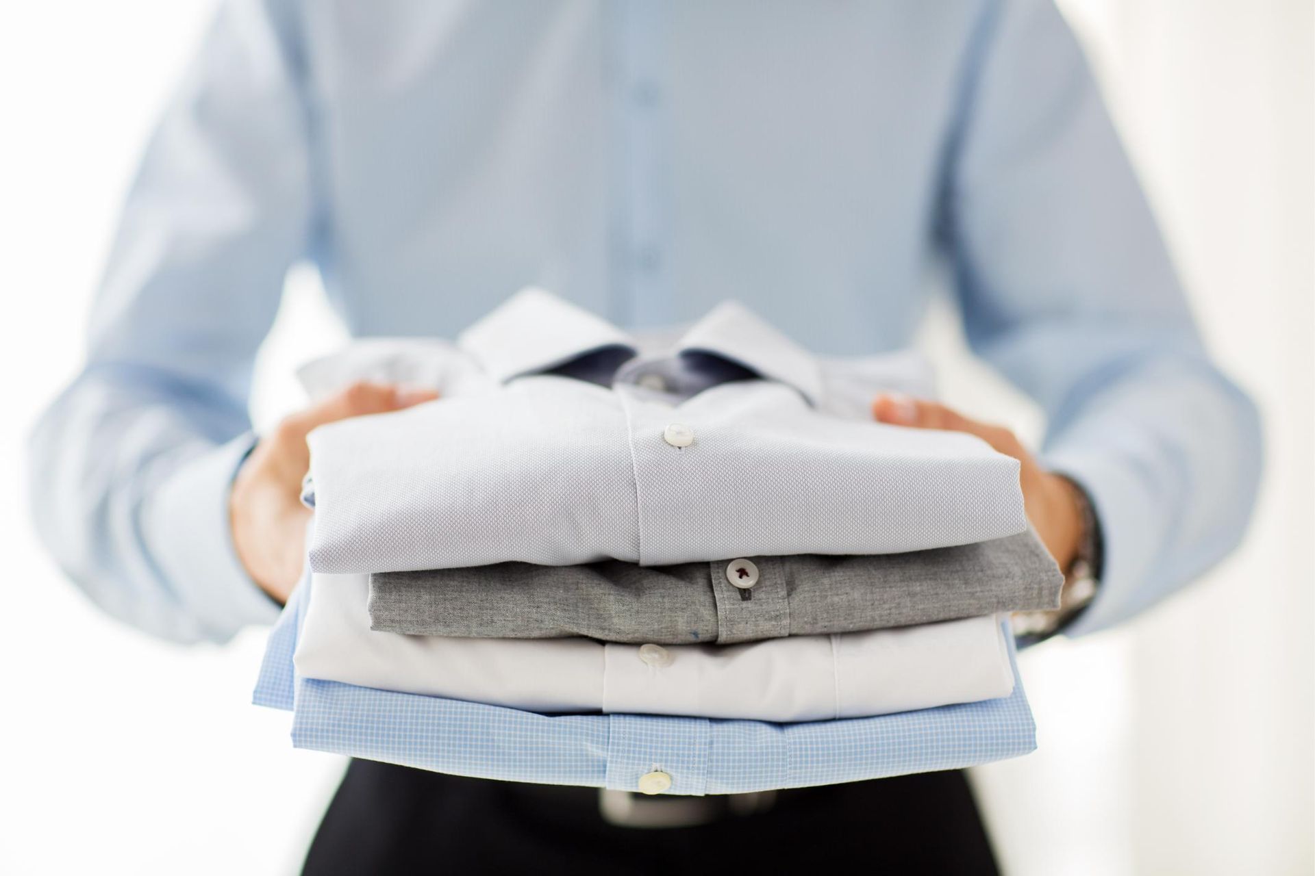 a man is holding a pile of folded shirts in his hands