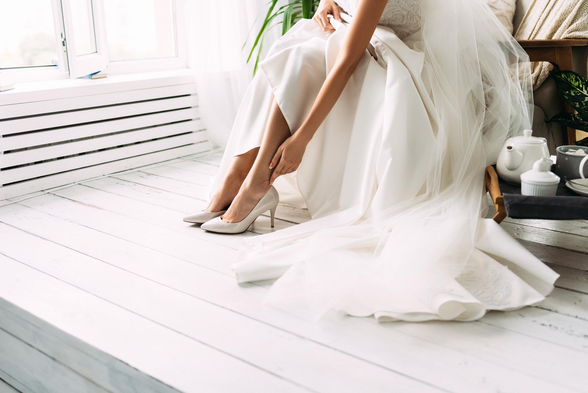 a woman in a wedding dress is sitting on a bench putting on her shoes