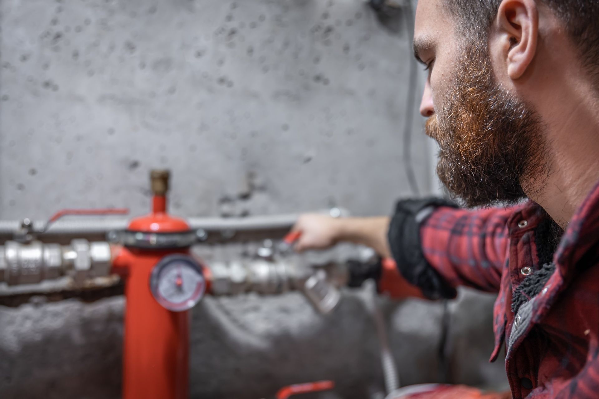 Hombre con camisa a cuadros ajusta válvulas en tuberías de agua rojas. Entorno industrial.