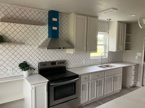 A modern kitchen featuring white cabinets, stainless steel appliances, a blue range hood, and a decorative tile backsplash.