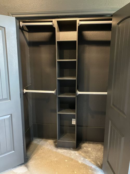 A charcoal grey closet with a central vertical shelving unit and horizontal rods for hanging clothes on both sides.