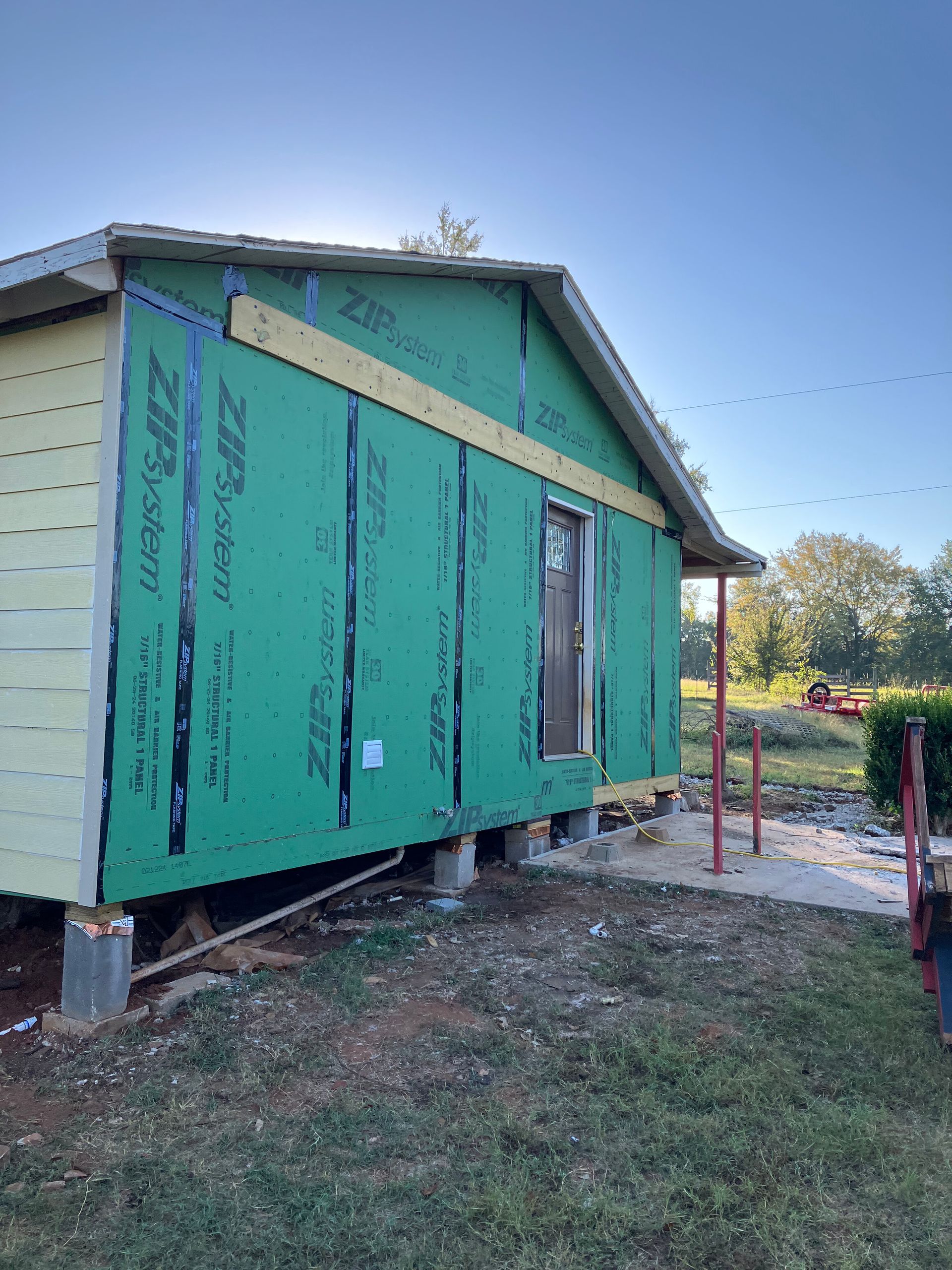 A small house under construction with green ZIP System wall sheathing, elevated on concrete block piers.