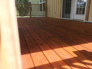 A close-up, low-angle view of a freshly stained reddish-brown wooden deck leading to a house door and railing.