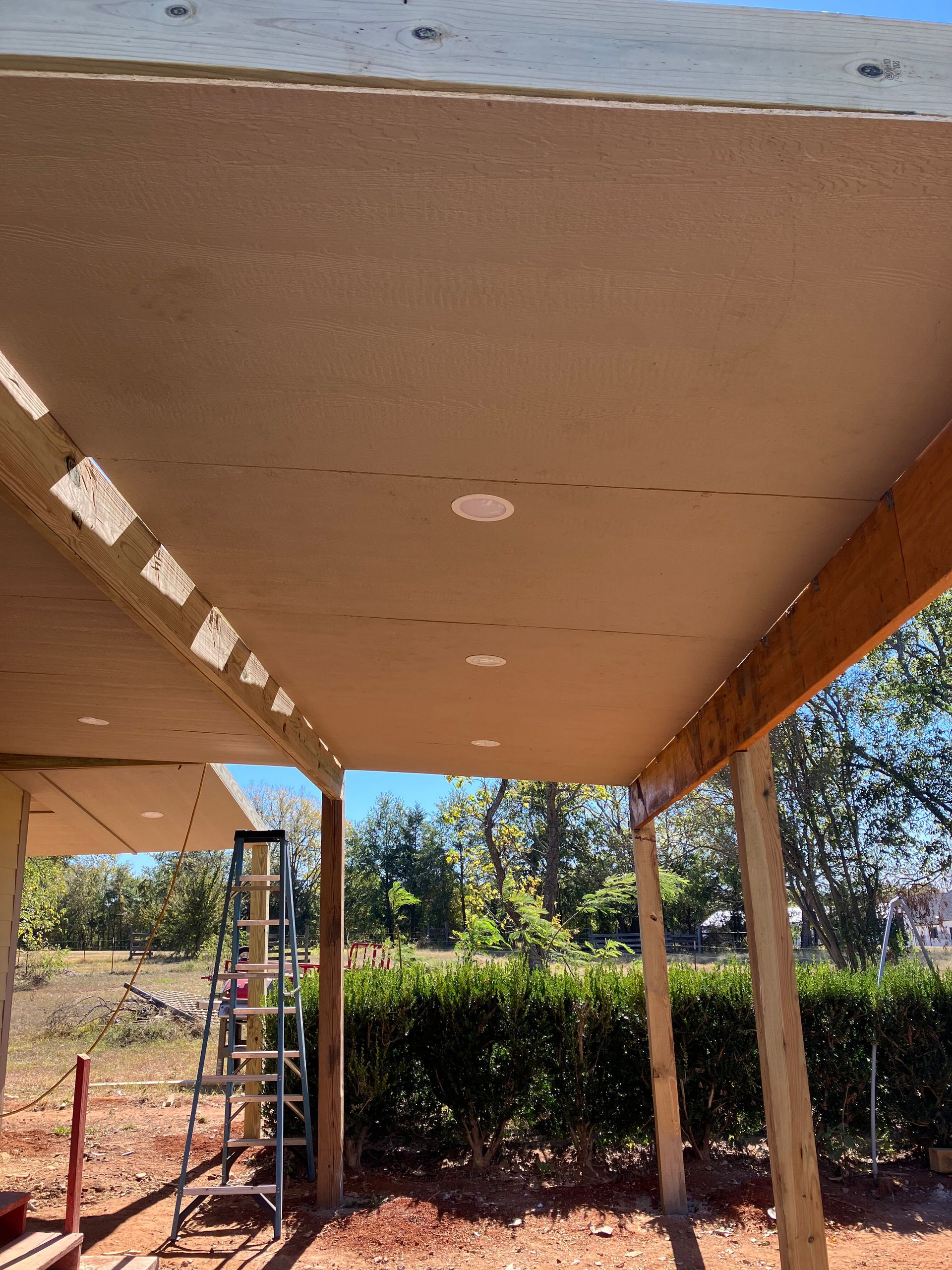 A view looking up at the wooden underside of a porch roof under construction, with a metal ladder visible to the left.