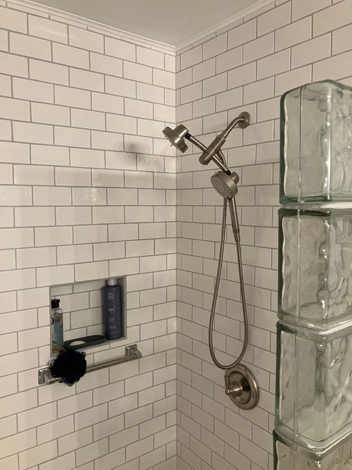 A shower with white subway tile walls, a built-in recessed shelf with toiletries, and a metallic showerhead fixture.