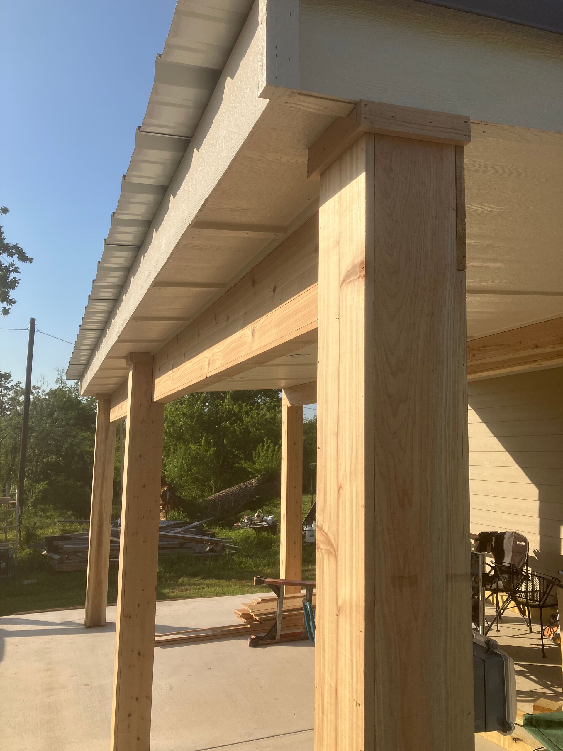 A low-angle view of a patio structure with wooden support beams holding up a metal roof against a clear blue sky.