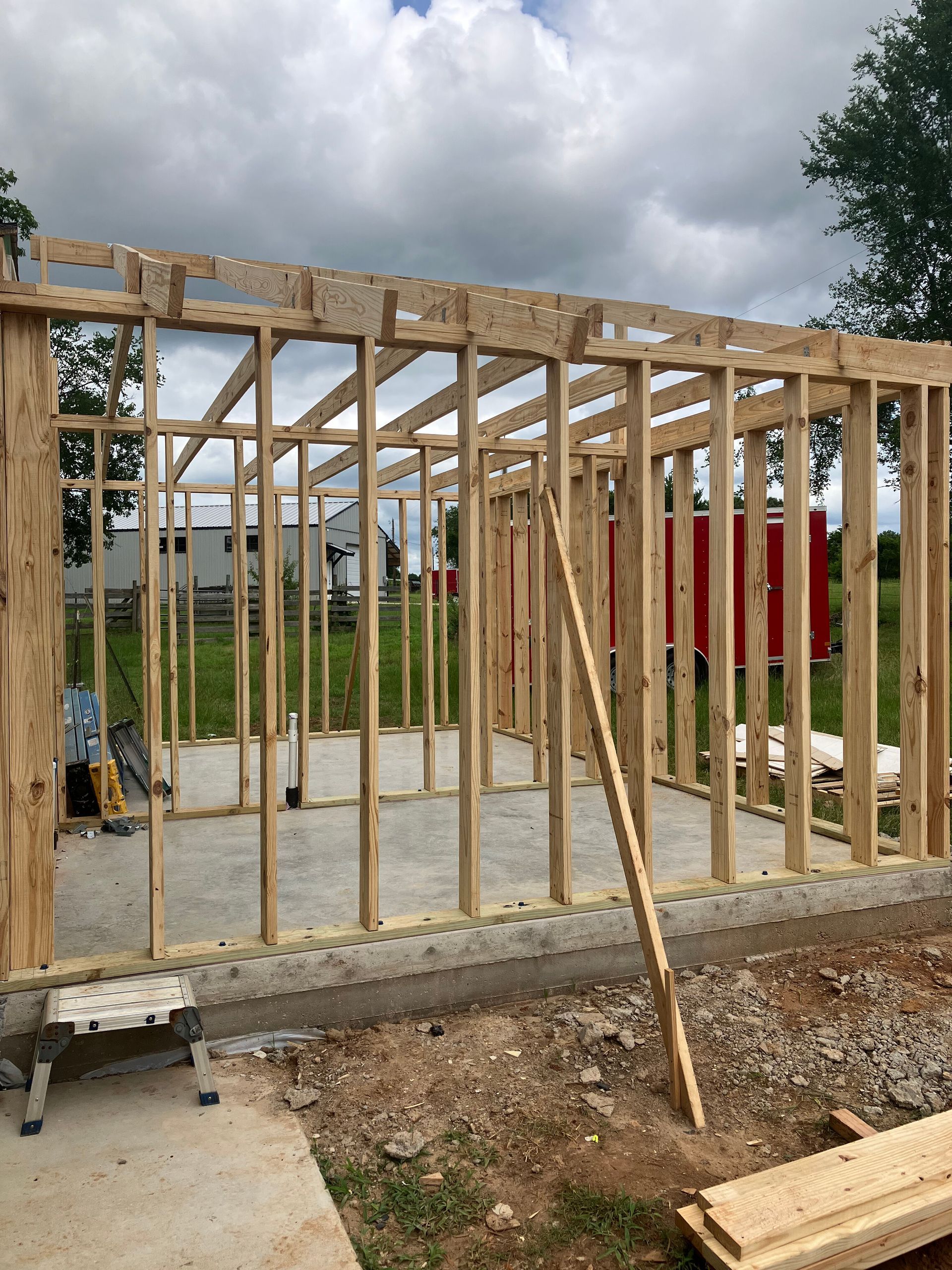 Wooden frame of a small building under construction, set on a concrete foundation in a grassy field.