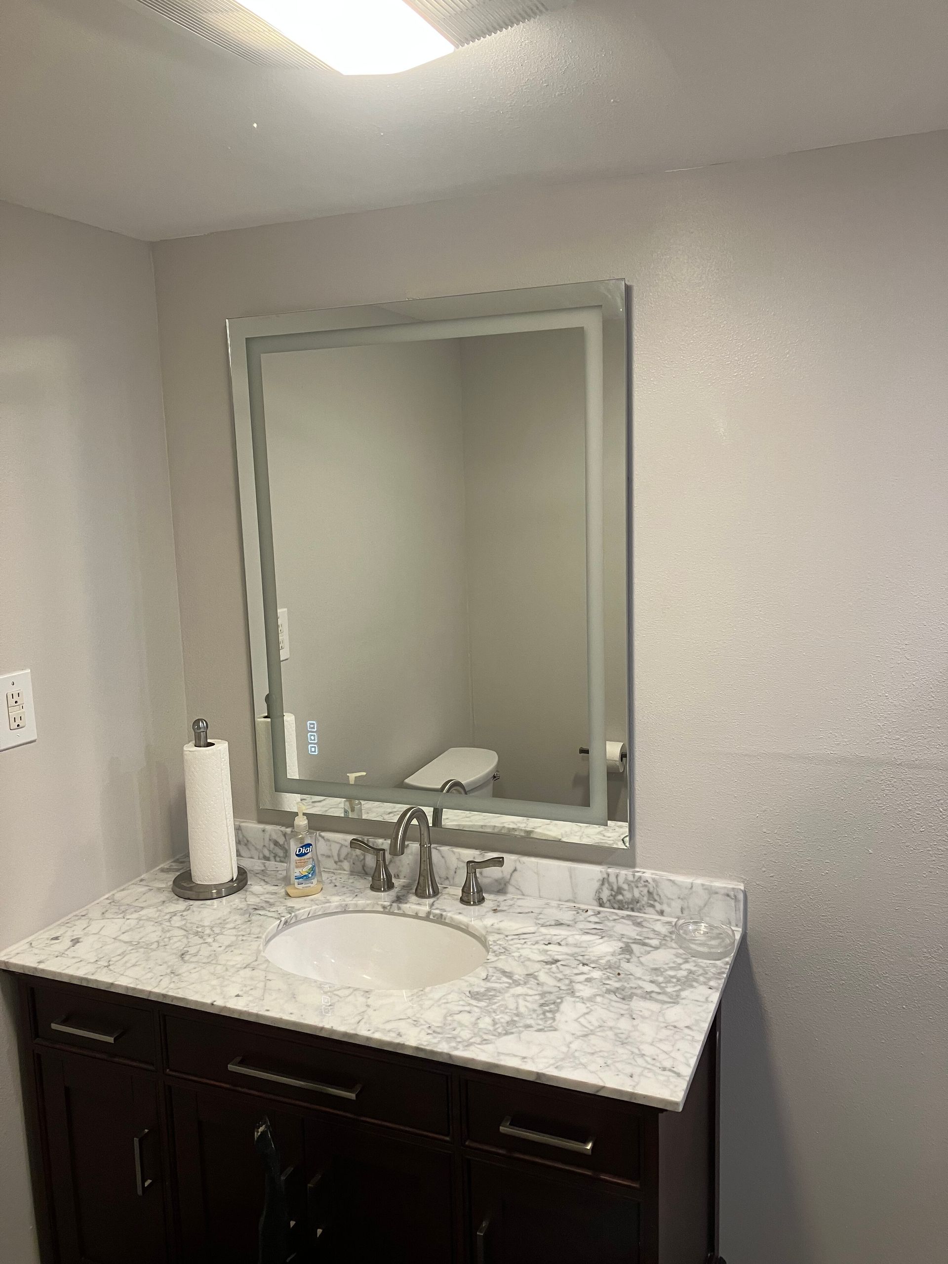 A bathroom vanity with a dark wood cabinet, white marble countertop, sink, faucet, and an illuminated rectangular mirror.