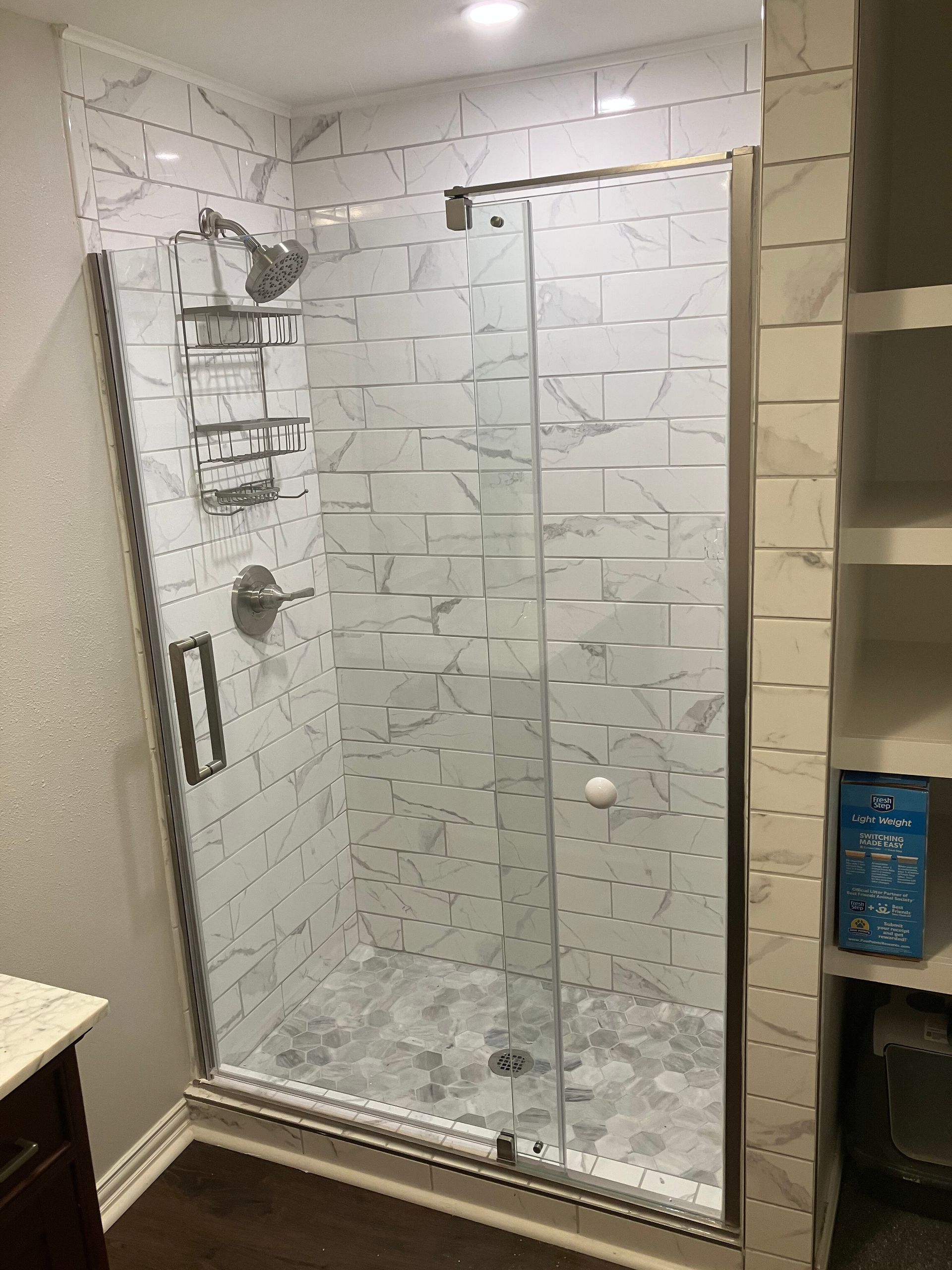 A walk-in shower with marble-look subway tile walls, a pebble-stone floor, a glass door, and chrome fixtures.