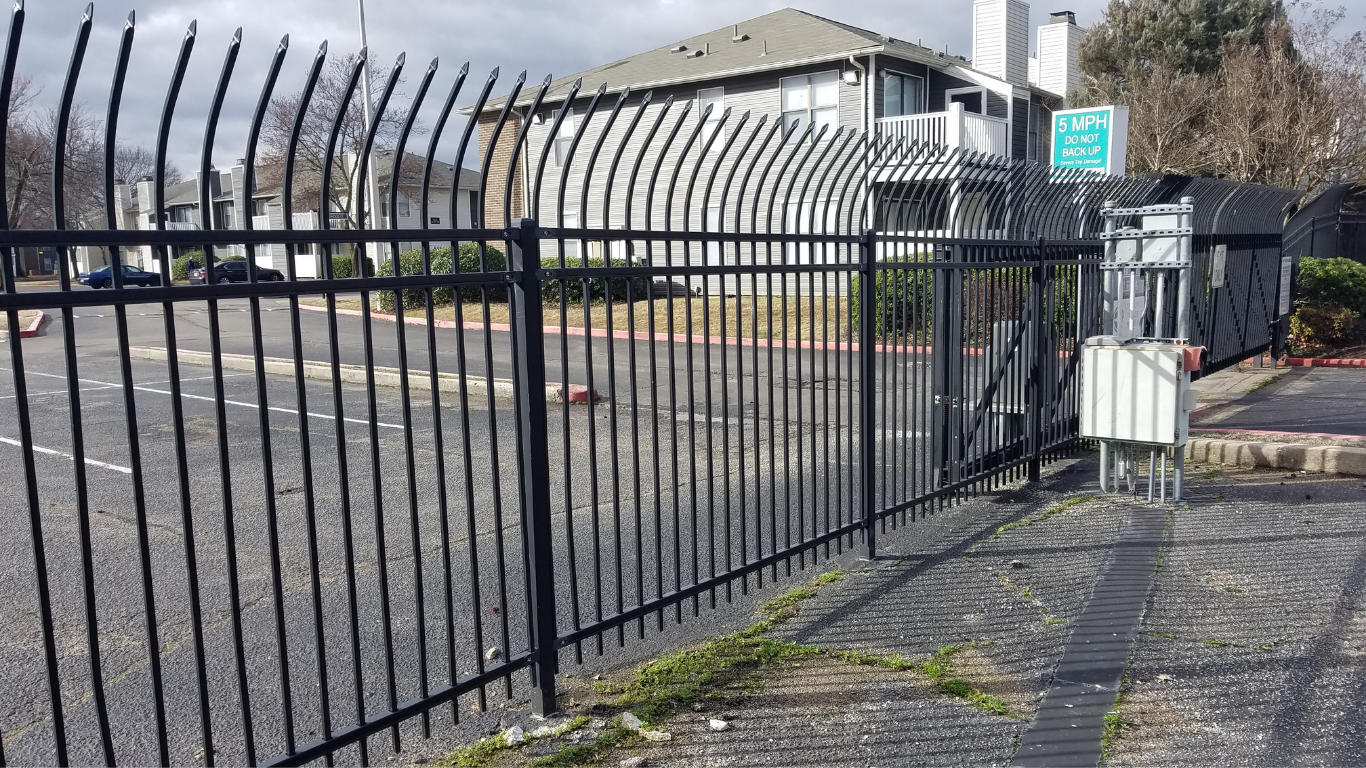 Black metal security fence in front of a residential building and a paved area.