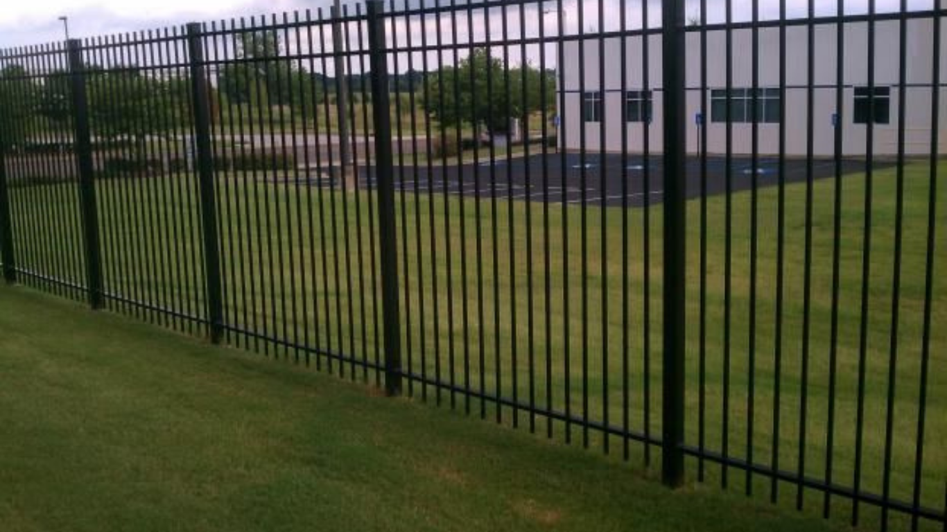 Black metal security fence on a green lawn, with a building and trees in the background.
