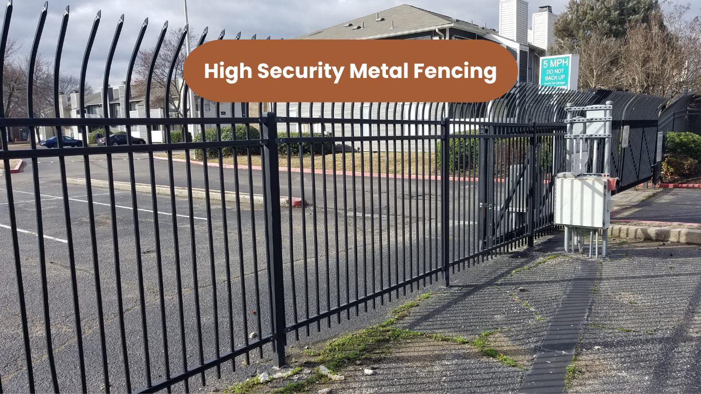 Black metal fence in front of a paved area and multi-story apartment building.