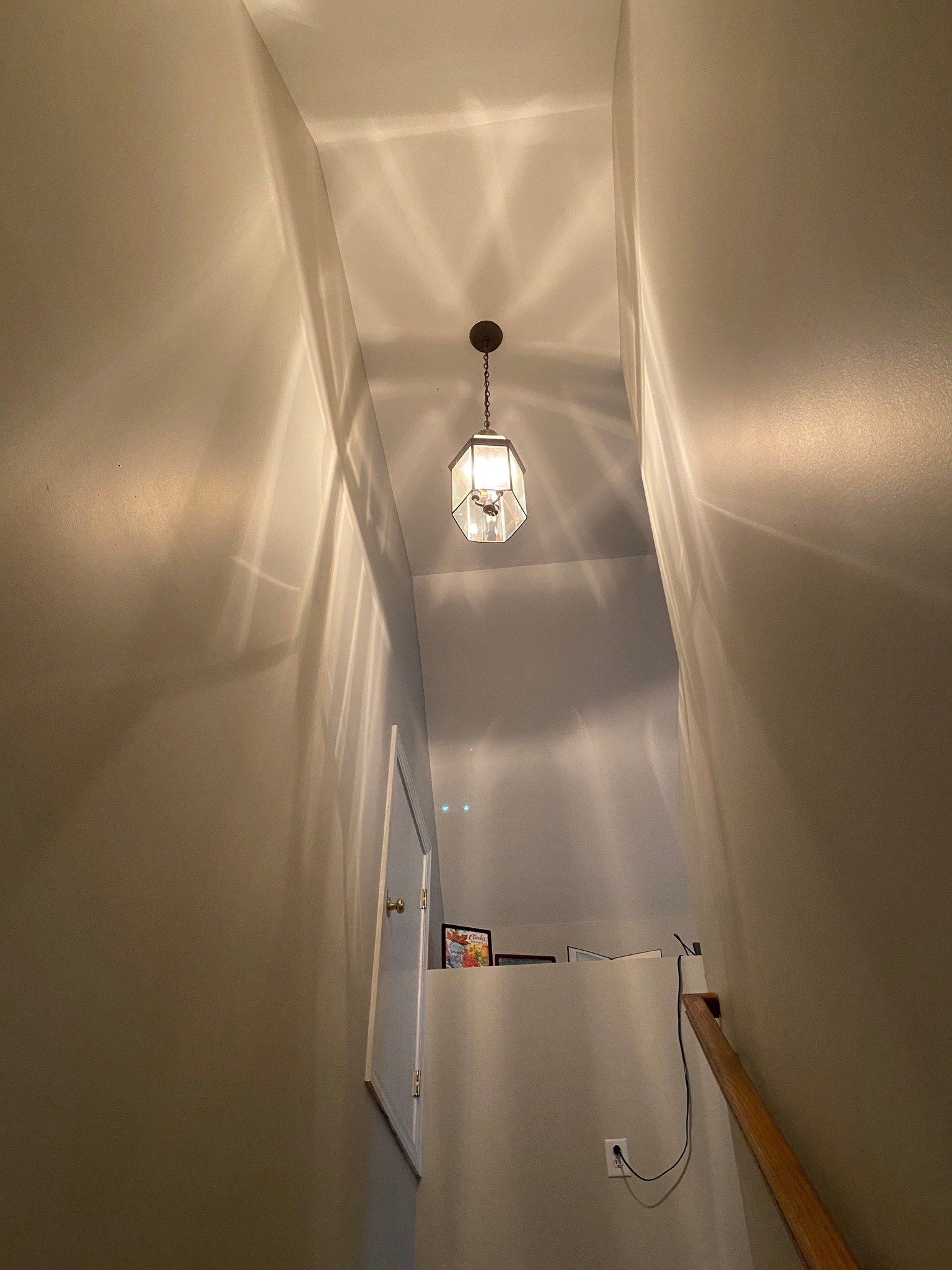 Stairwell with a hanging light fixture casting patterned shadows on the walls.