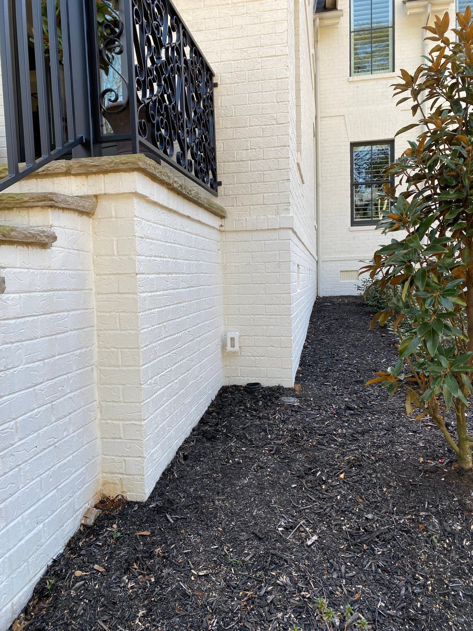 White brick building with black mulch and decorative iron railing.