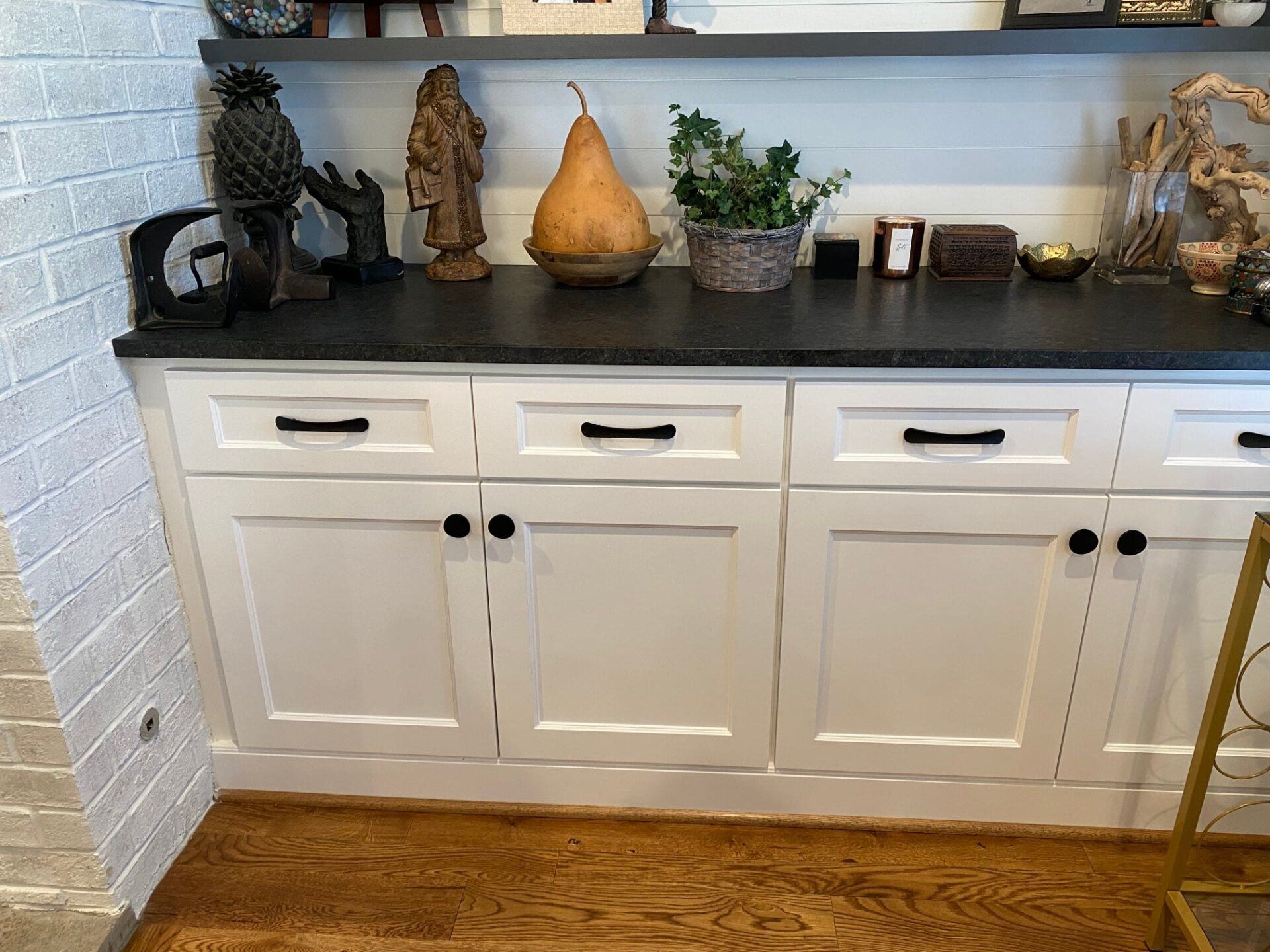 White cabinets with black countertop, various decor on top shelf, hardwood floor.