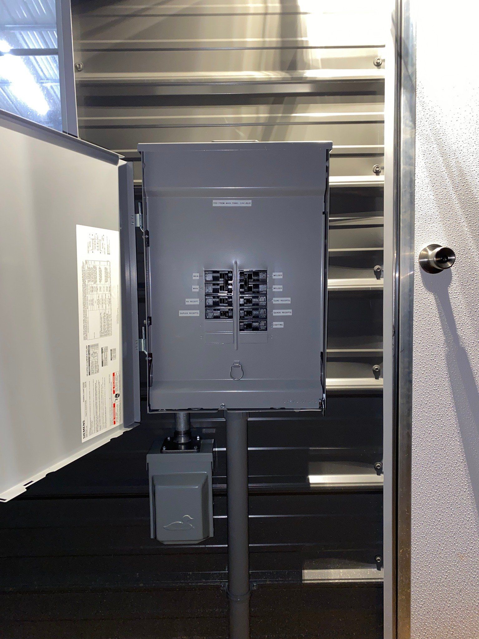 Gray electrical panel with exposed breakers, mounted on a pole inside a metal enclosure.