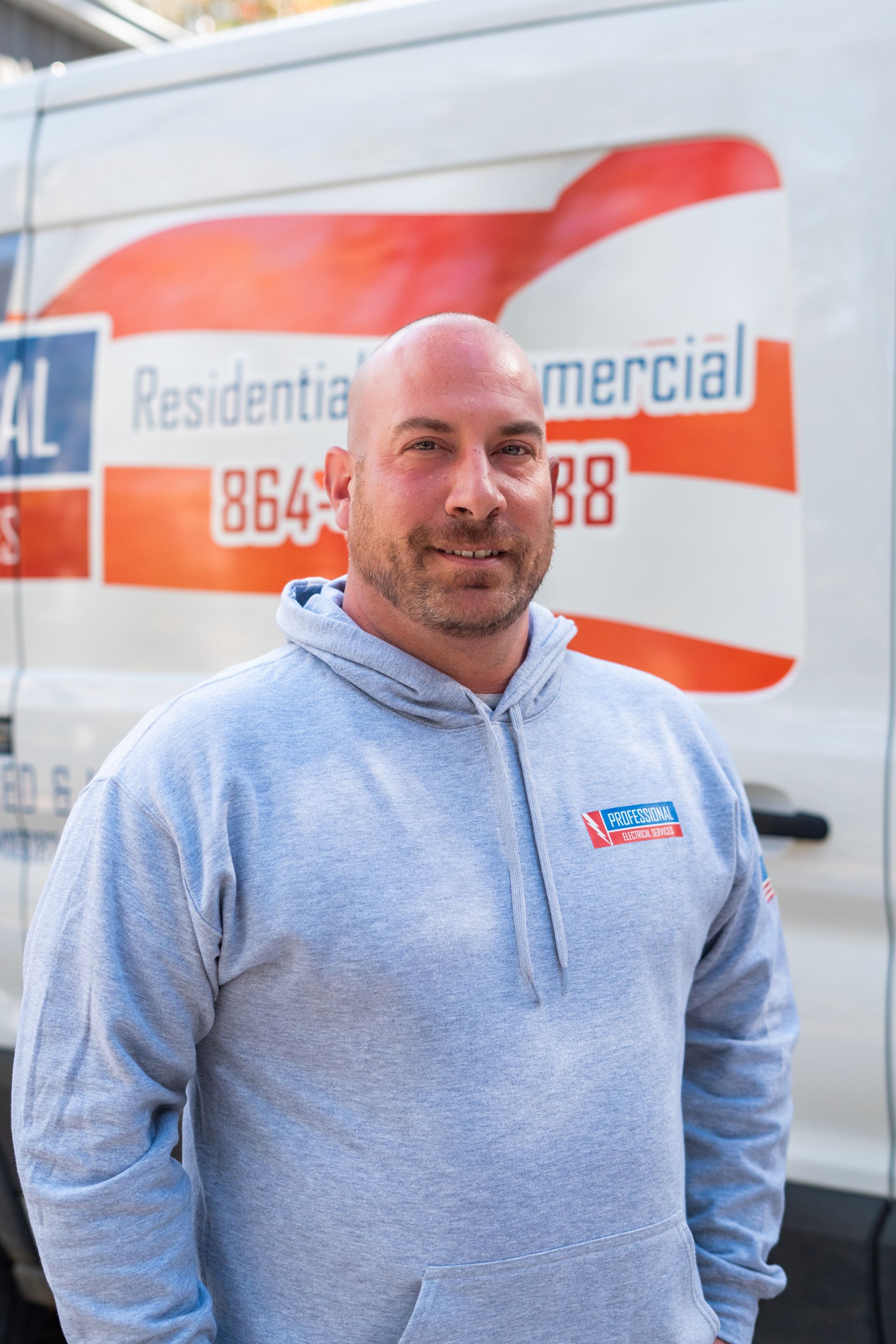 Man in gray hoodie in front of a white van with business logo.