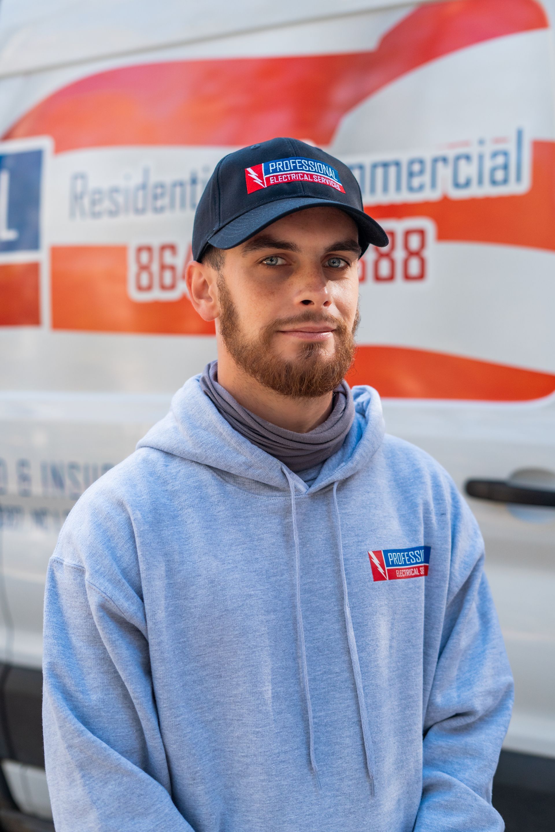 Man in a gray hoodie and cap stands in front of a commercial van. He has a slight smile.