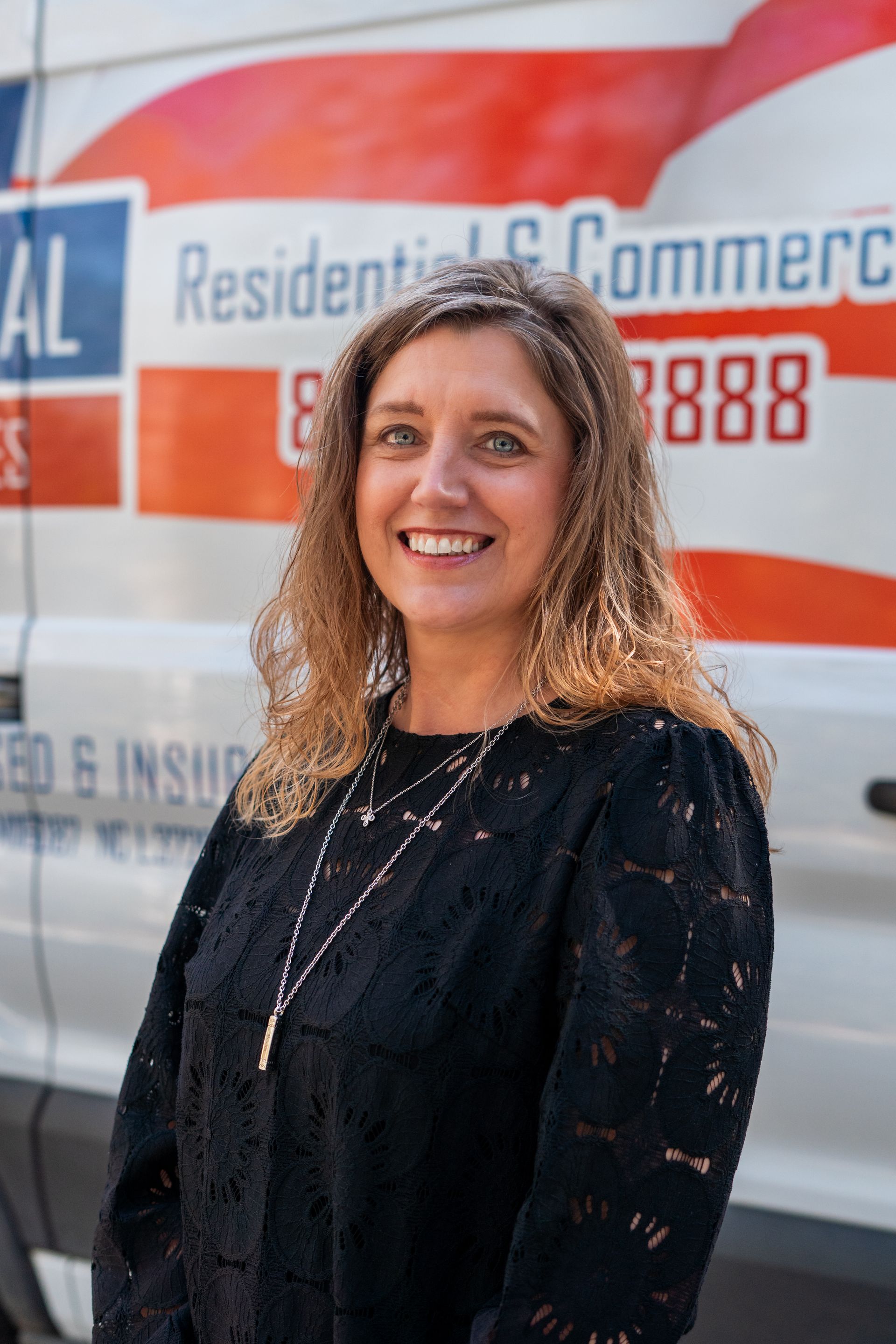 Woman smiling, standing in front of a white van with red and blue lettering that says 