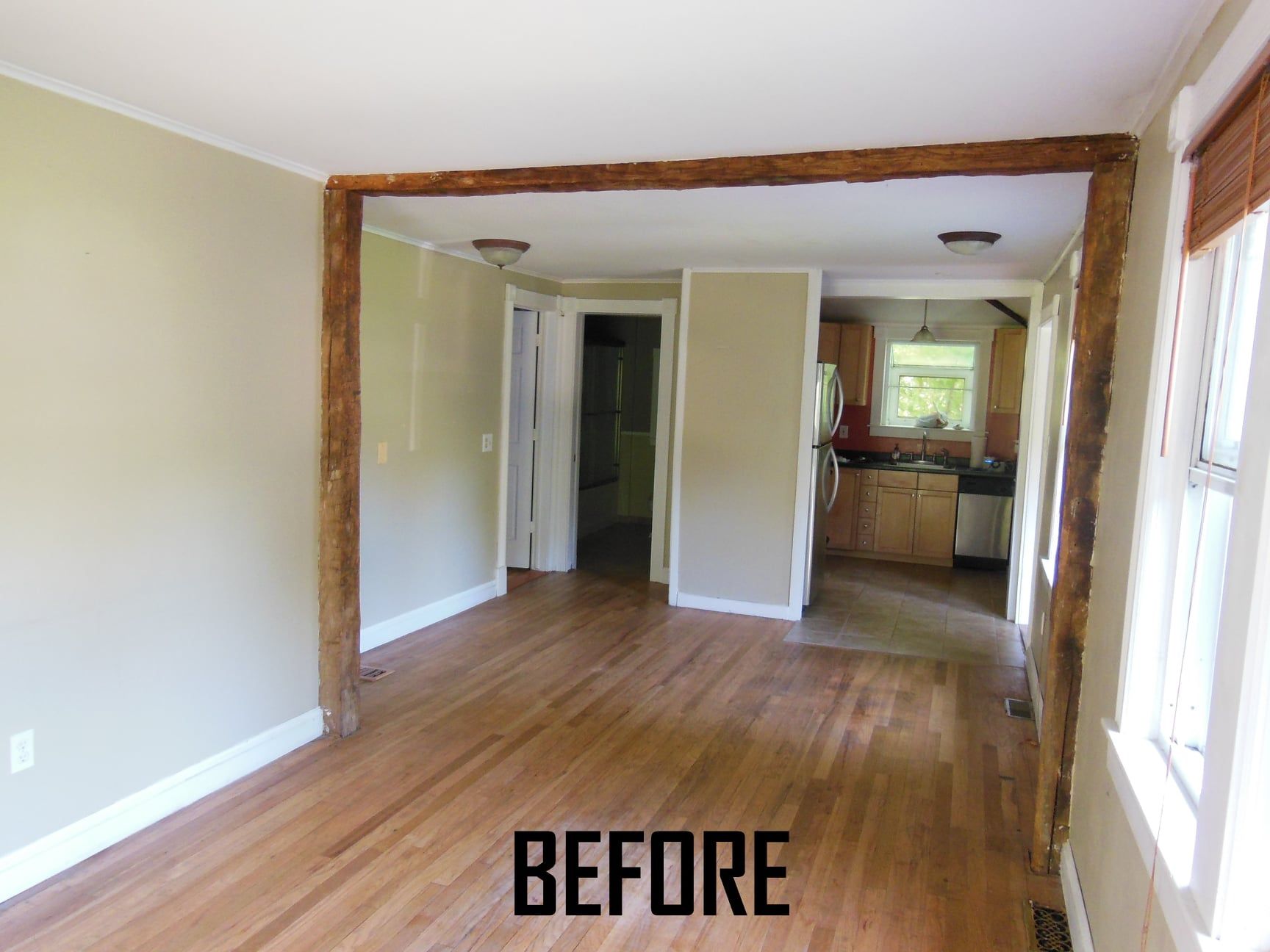 Interior view of a room with hardwood floors and beige walls, a doorway with wood trim, and a glimpse into the kitchen.