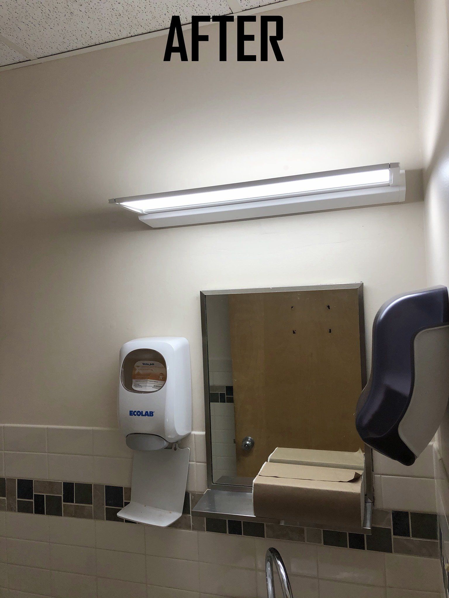 Public restroom with mirror, paper towel and soap dispensers, and fluorescent lighting.