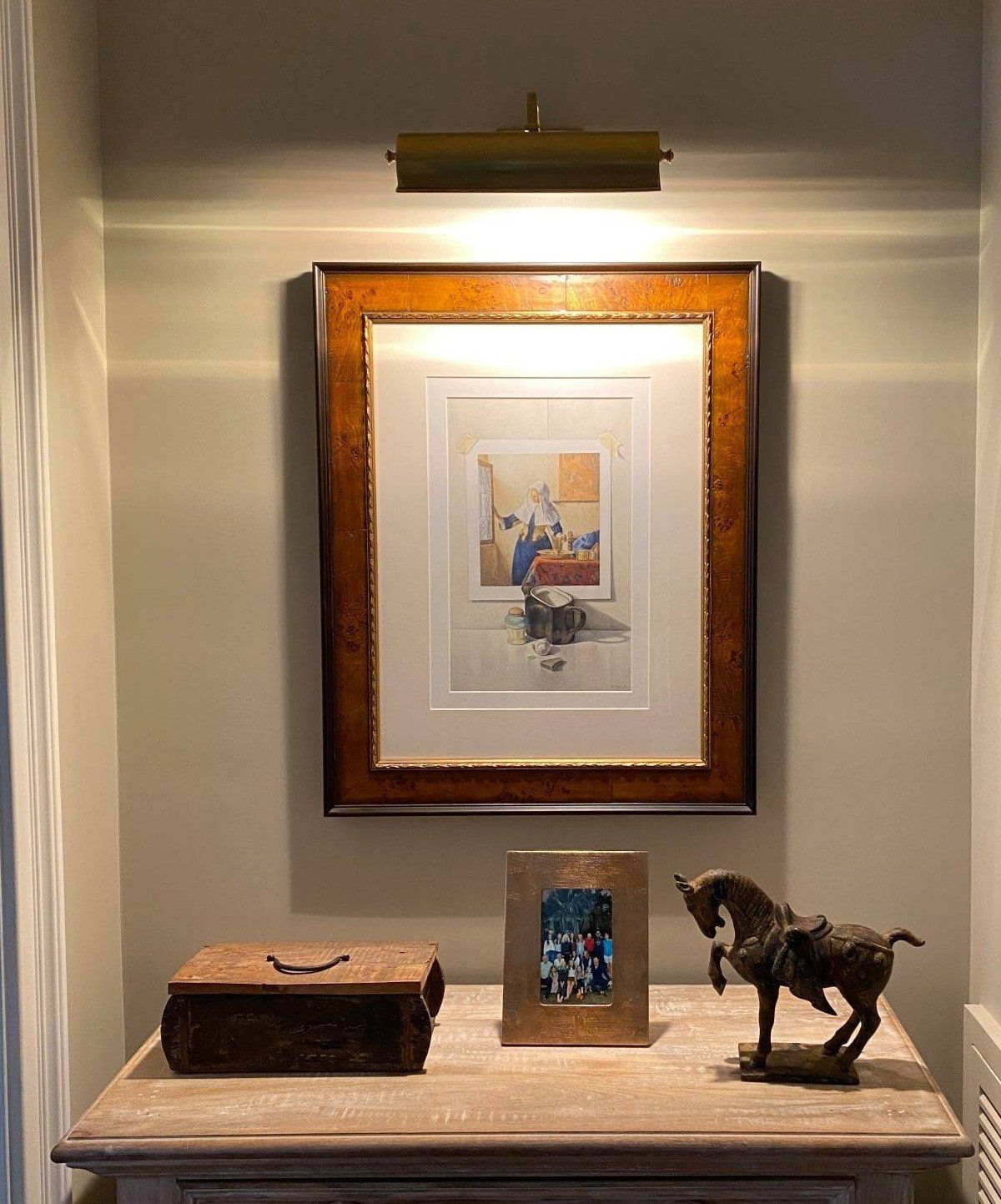 A lit artwork with frame, box, framed photo, and horse statue on a wooden table, against a light wall.