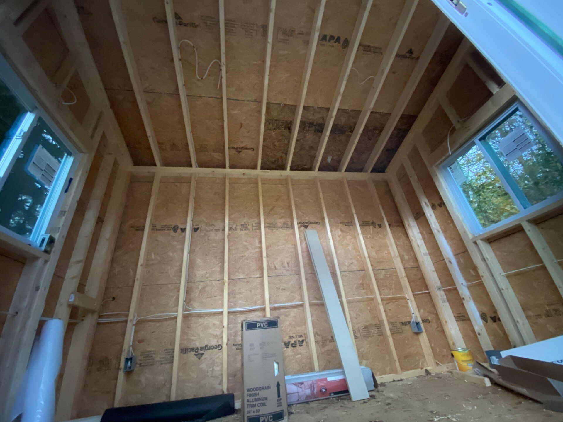 Interior framing of a room with exposed wooden studs, windows, and ceiling beams; construction site.