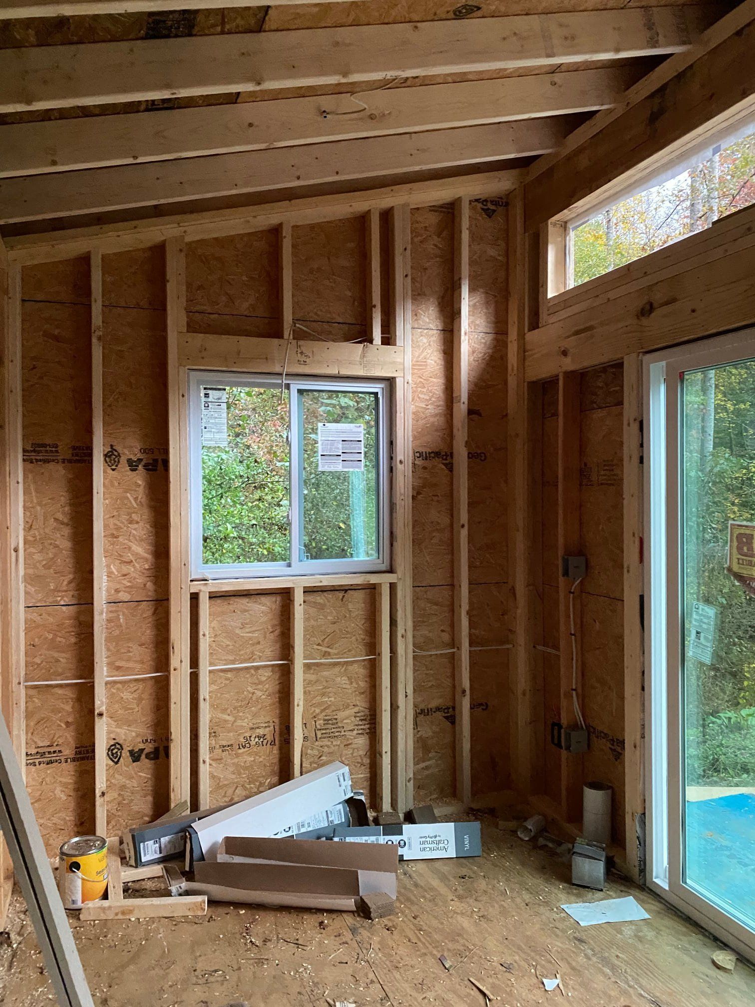 Interior of a room under construction, with wooden framing, windows, and tools on the floor.
