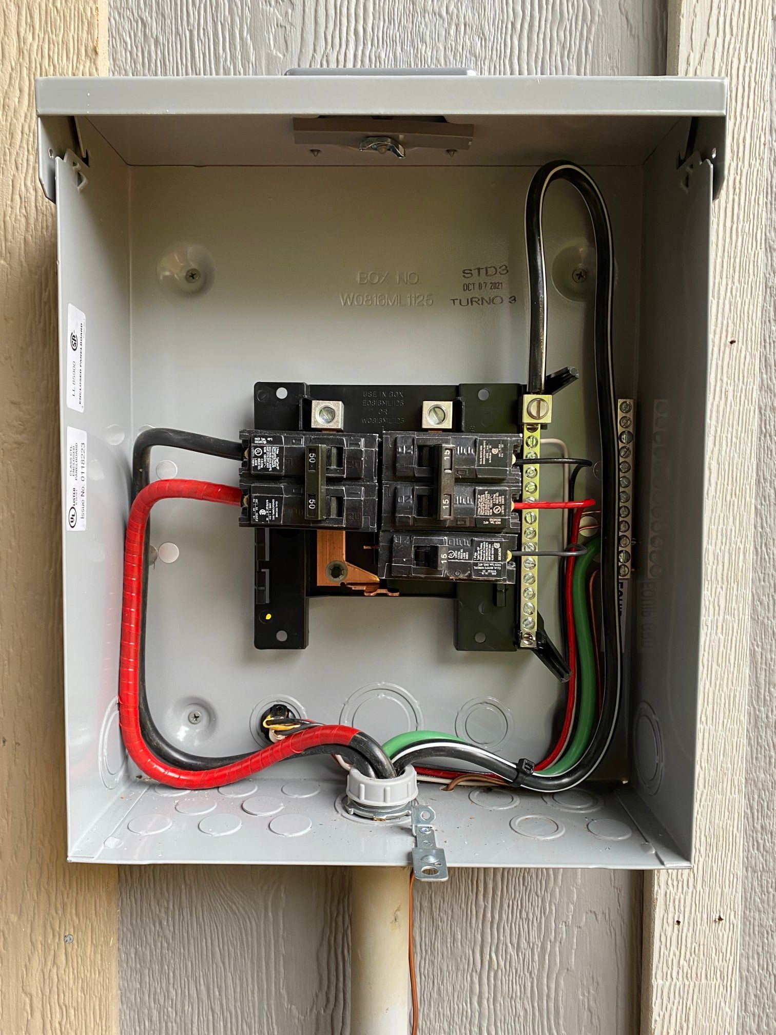 Open electrical panel with black and red wires, and circuit breakers. Green and white wires are visible.