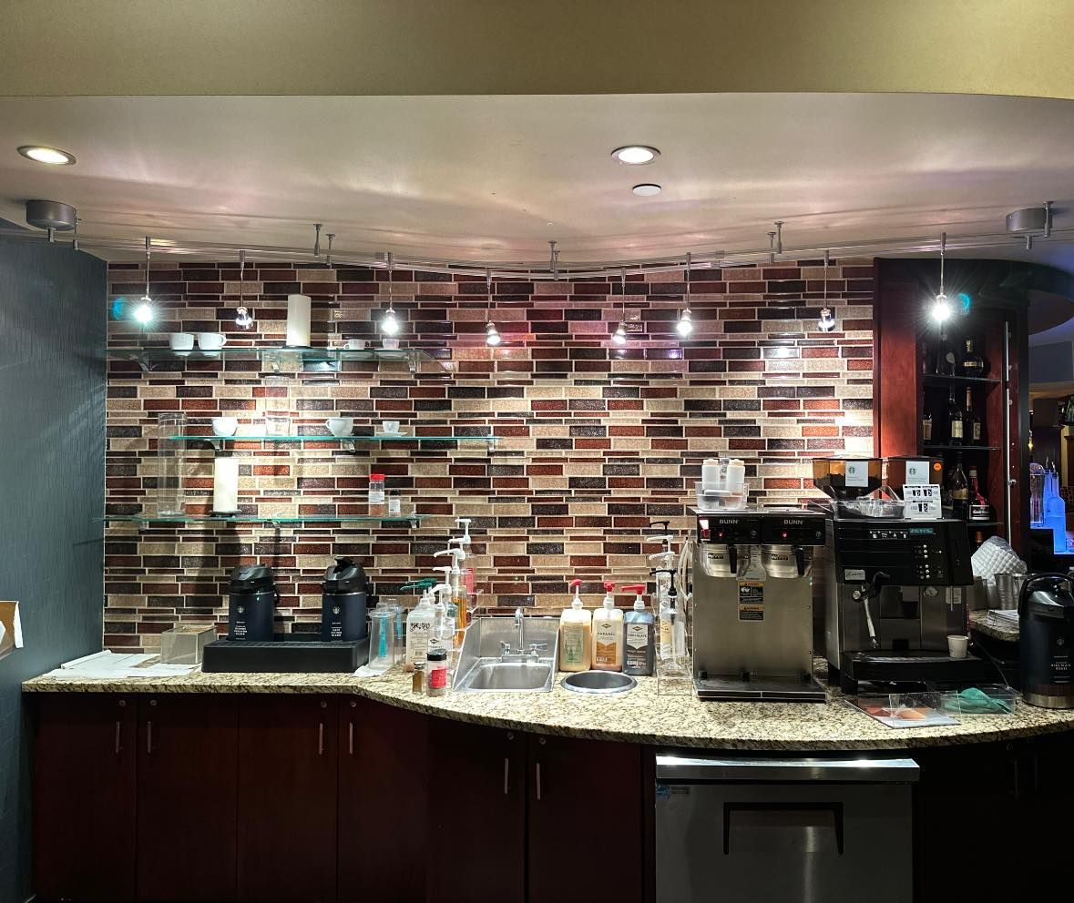 Coffee bar with brown brick tile backsplash, espresso machine, and bottles.