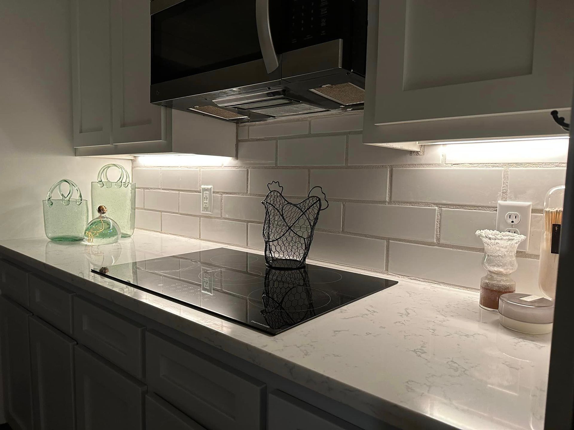 Kitchen counter with stove, white cabinets, and subway tile backsplash; glass decor.