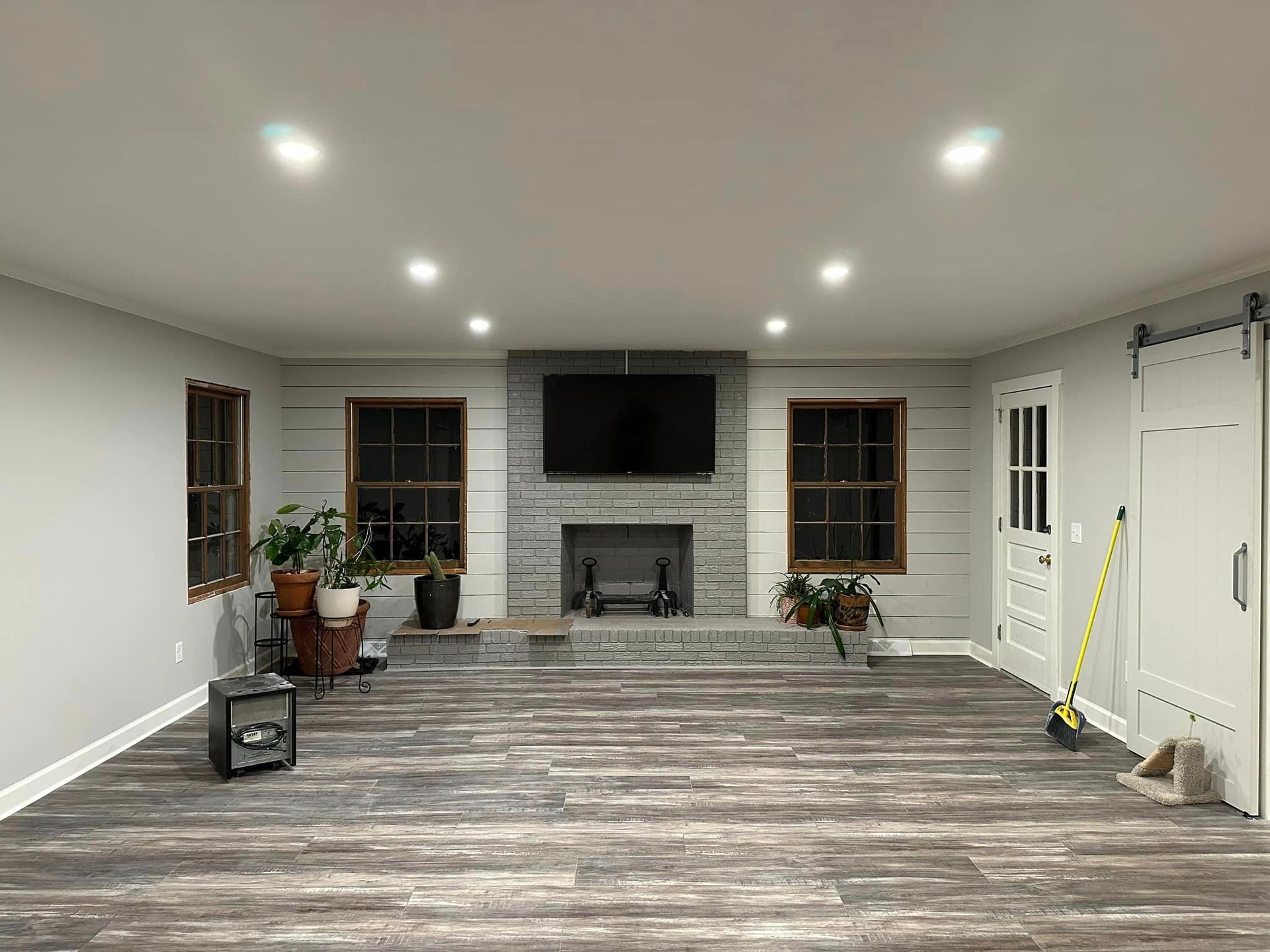 Empty living room with fireplace, TV, wood floors, recessed lighting, and a sliding door.