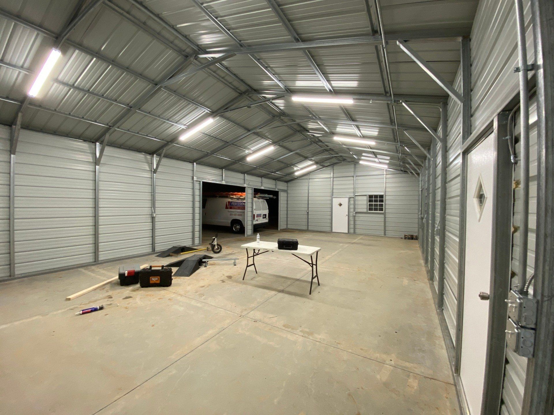 Inside of a large metal building. Table and tools on the floor. Van visible in the distance.
