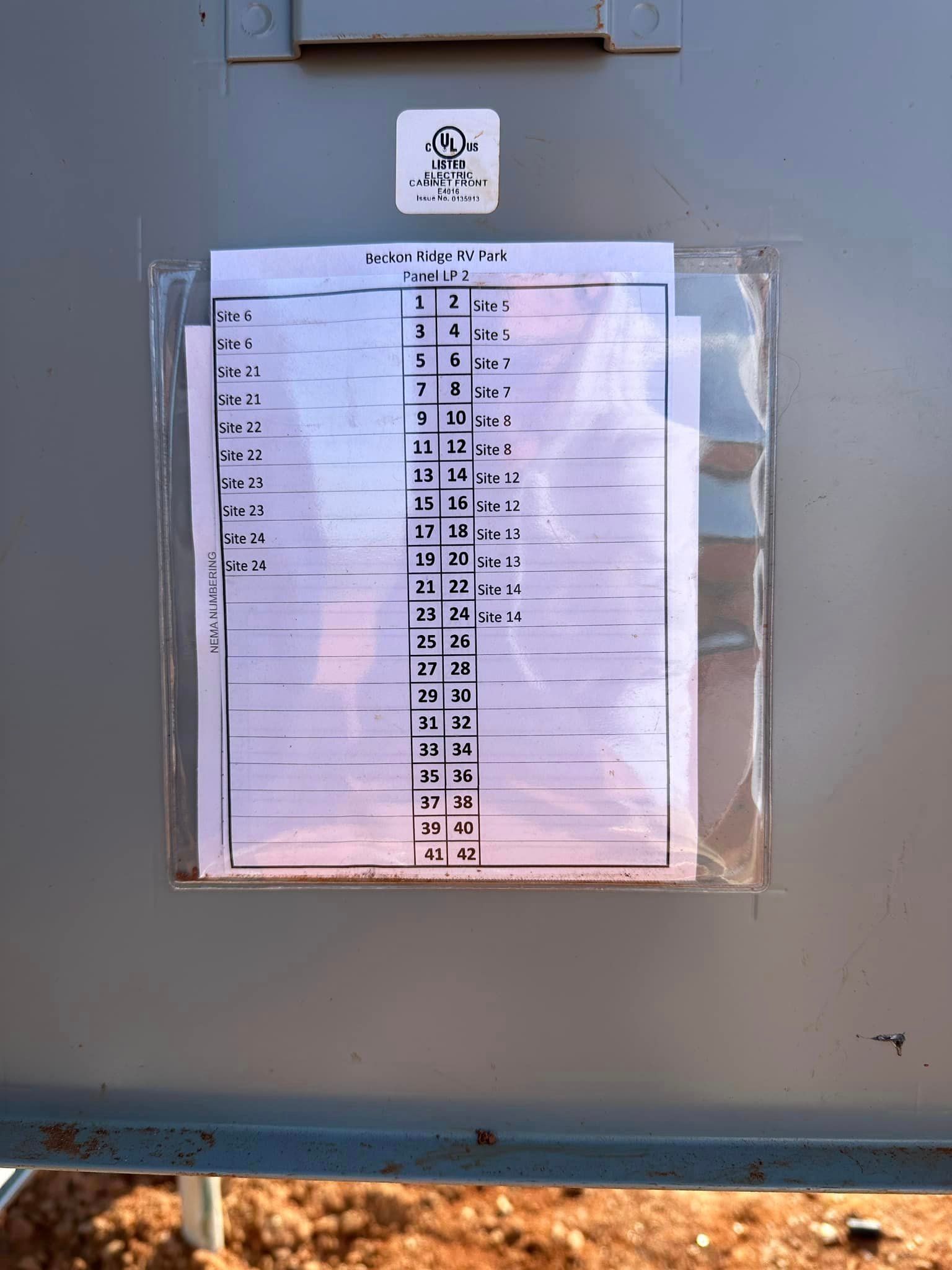 Gray metal box with documents in a plastic sleeve, likely an electrical panel outdoors.