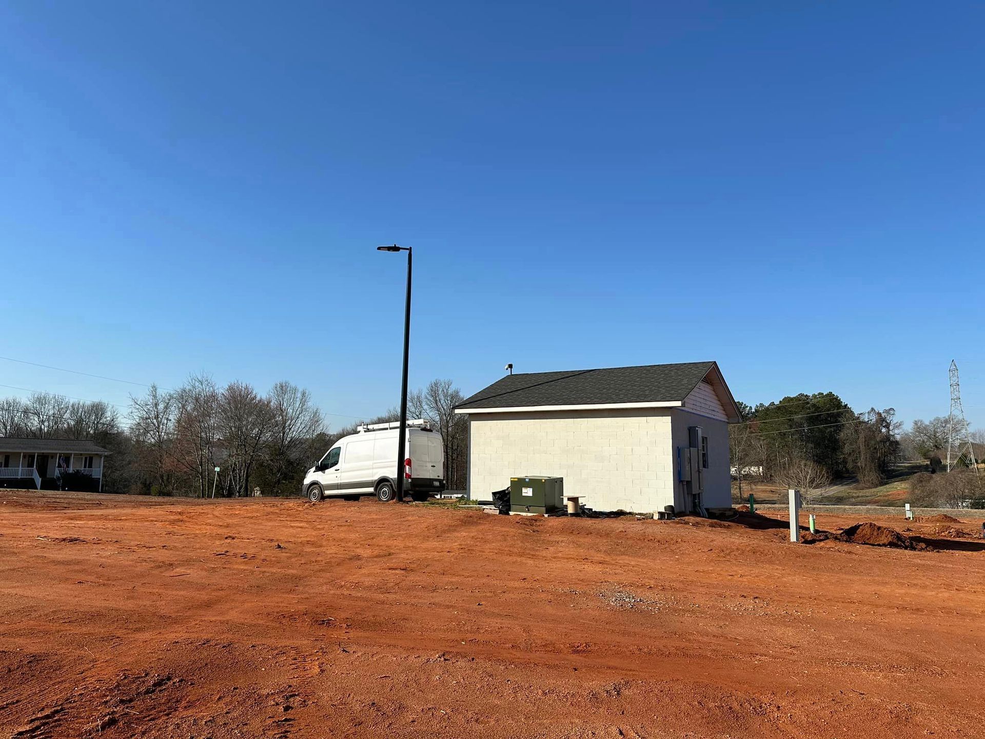 Construction site with small building, van, and red dirt under a blue sky.
