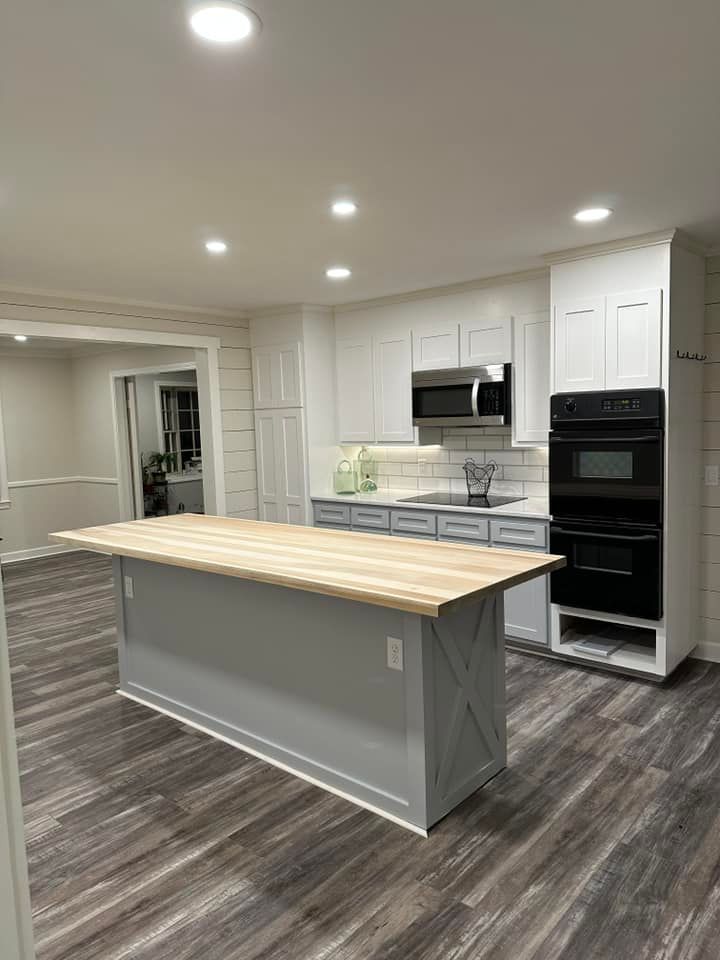 Modern kitchen with gray island and light wood countertop, white cabinets, and dark appliances.