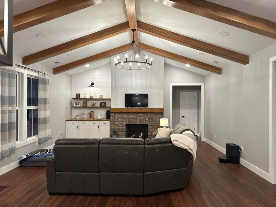 Living room with exposed wood beams, brick fireplace, leather couch, and dark wood flooring.
