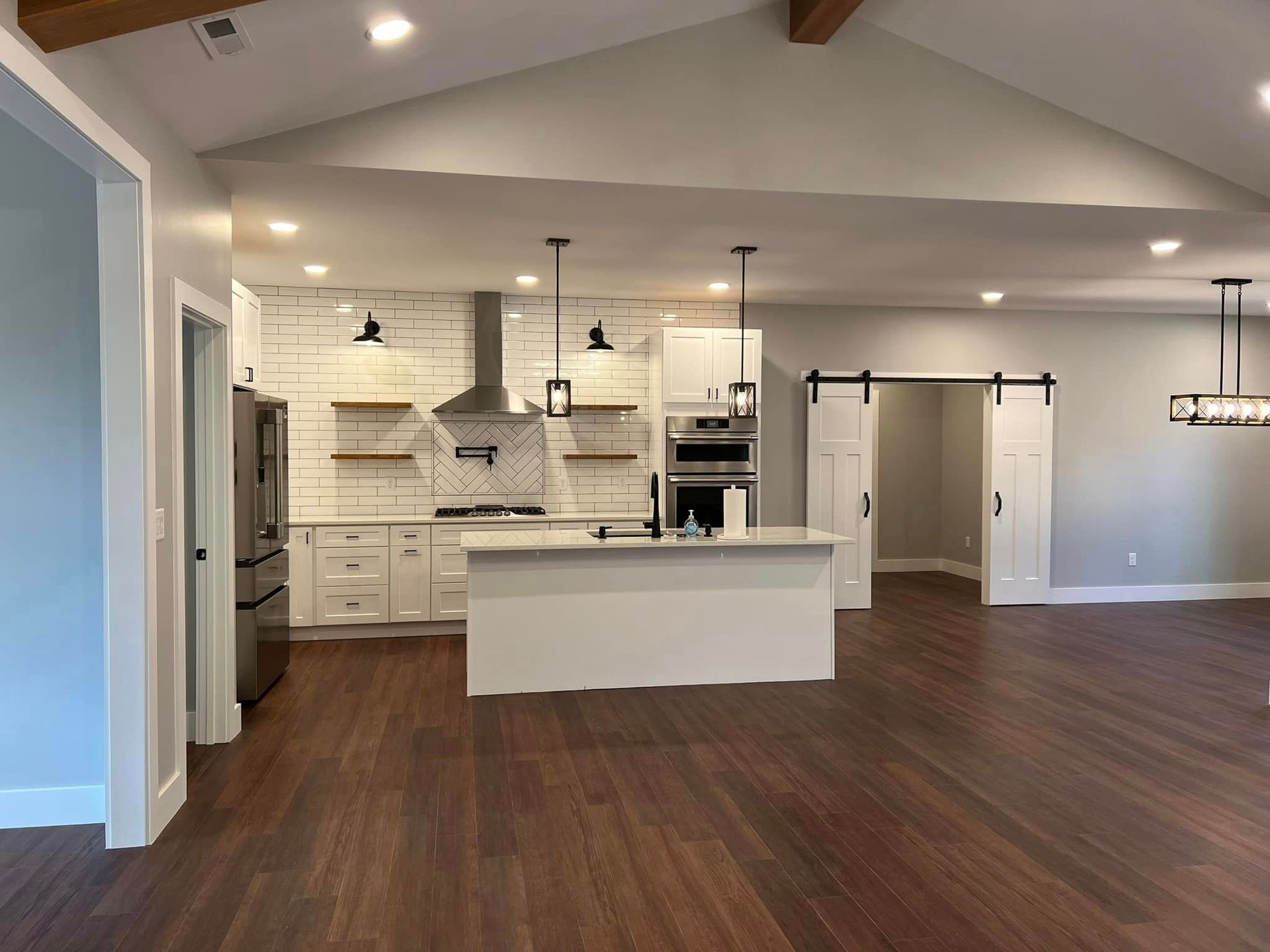 Open-concept kitchen with white cabinets, island, and brick accent wall; dark wood floors, pendant lights.